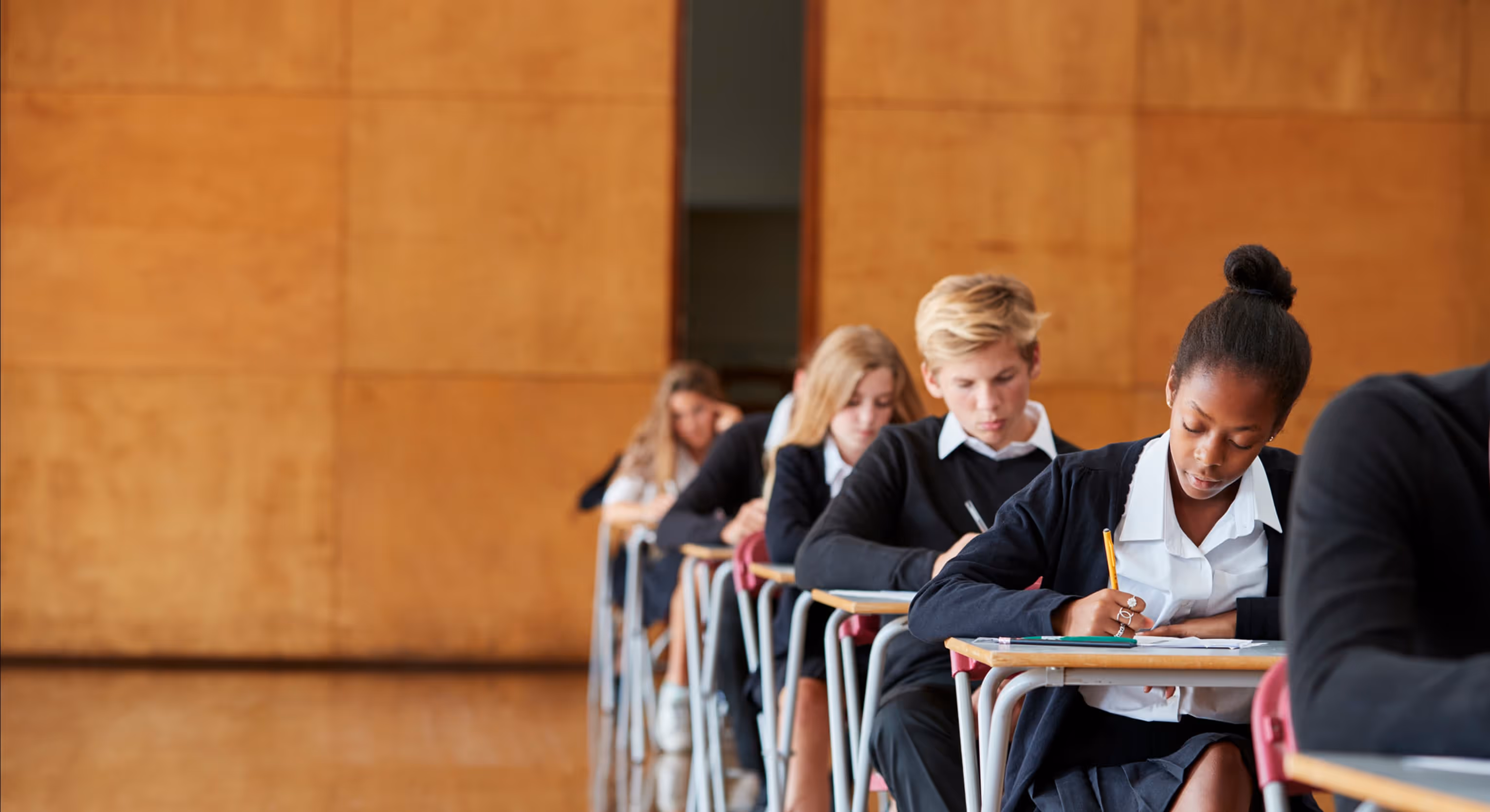 Students in school uniforms sitting at desks in a classroom, focused on writing.