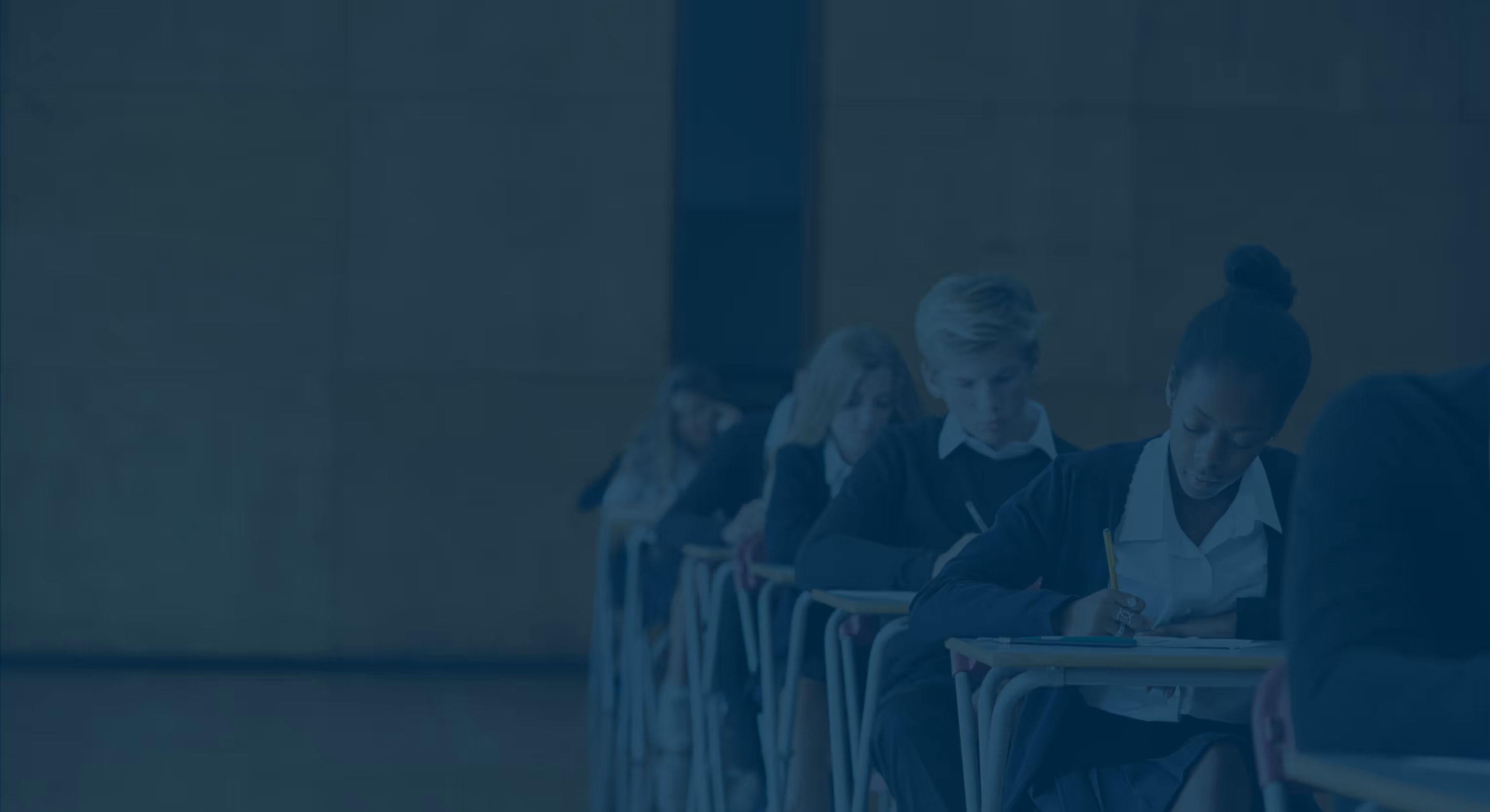 Students sitting in a classroom, focused on writing at their desks.