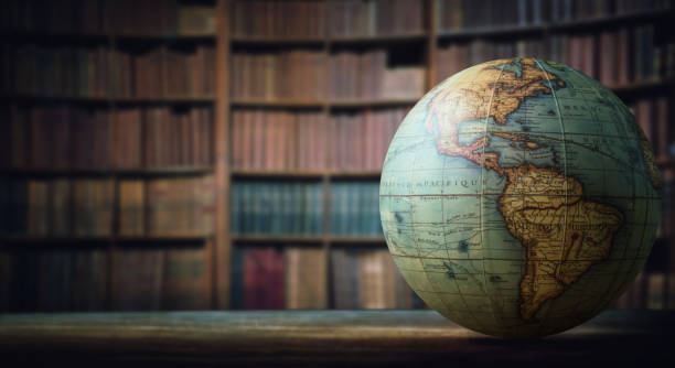 A globe sits on the right side of a desk in front of a bookshelf. 