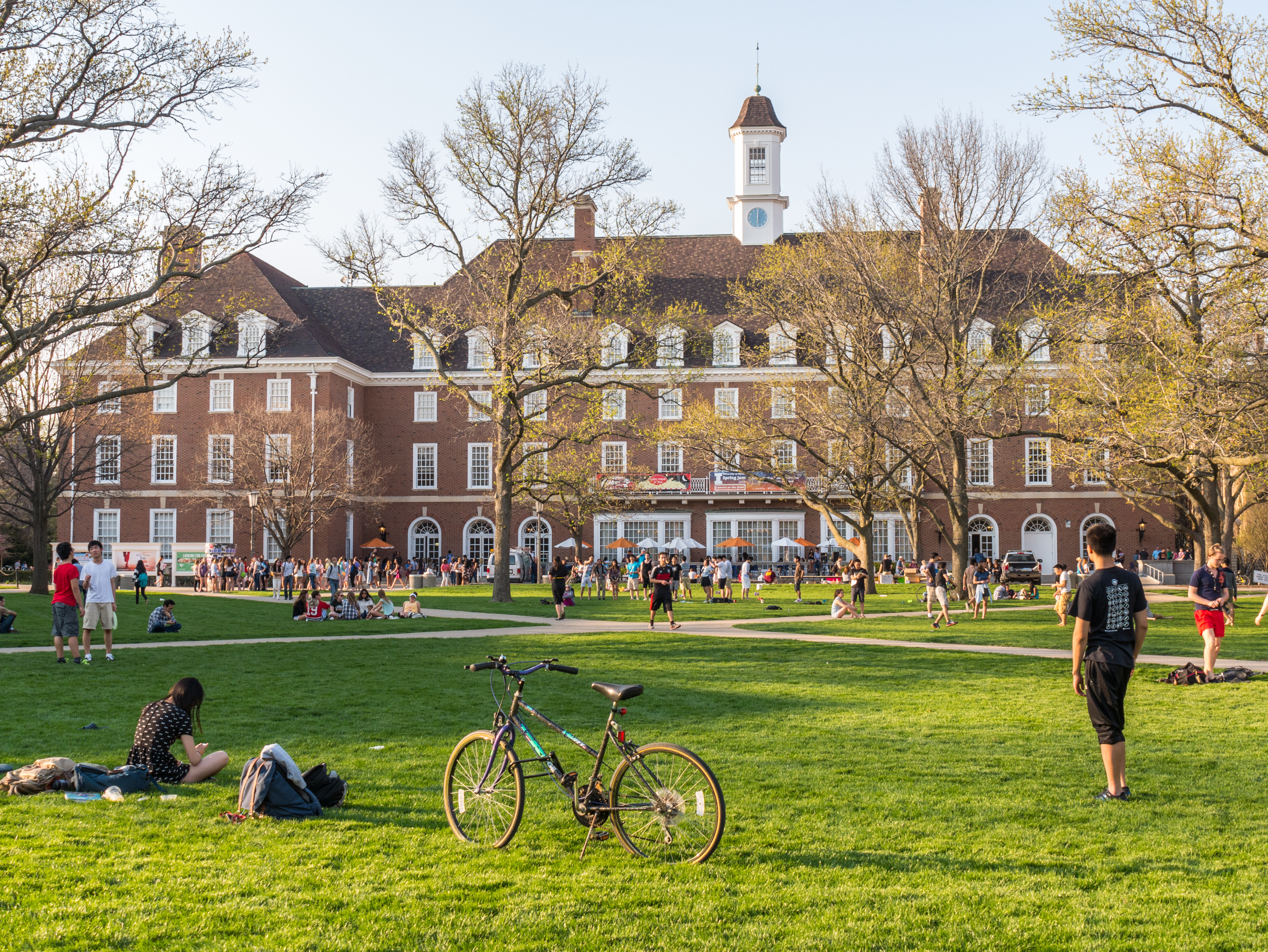 Students relax and walk on a green with a college building in background. 