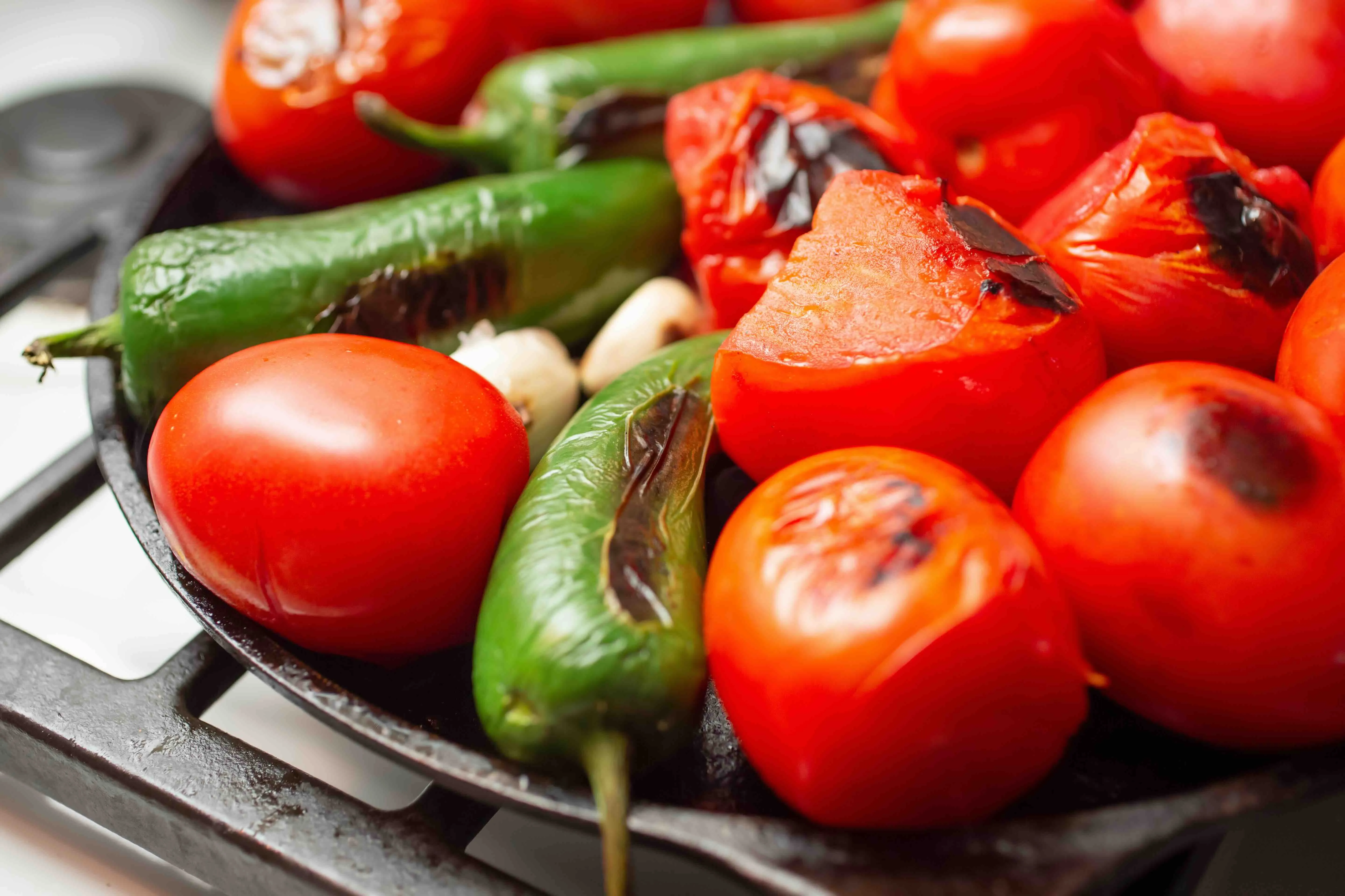 Tomatoes, garlic, and jalapeños roasting on a cast iron comal.