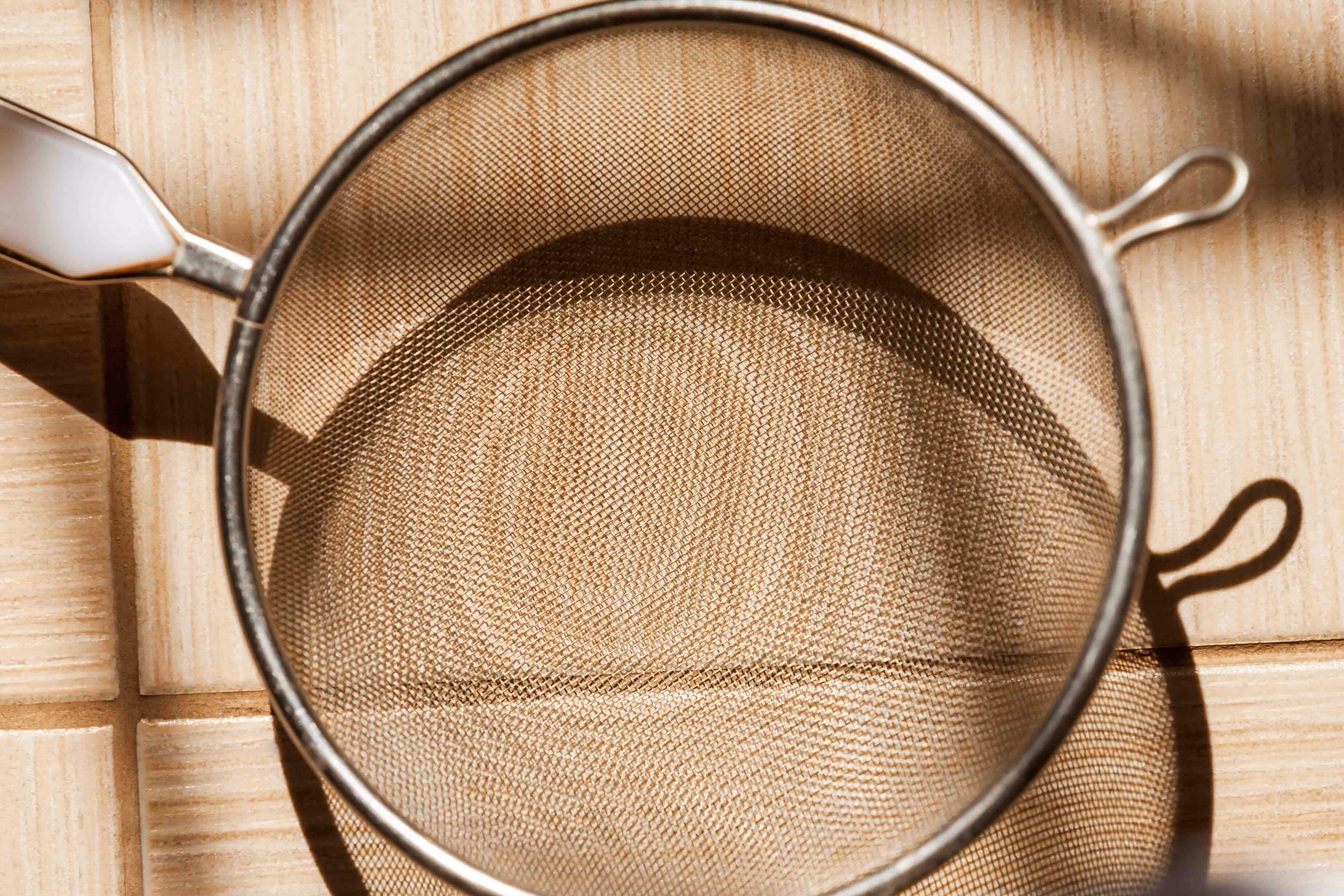 Close-up of a mine-mesh metal strainer sitting on a tile countertop.