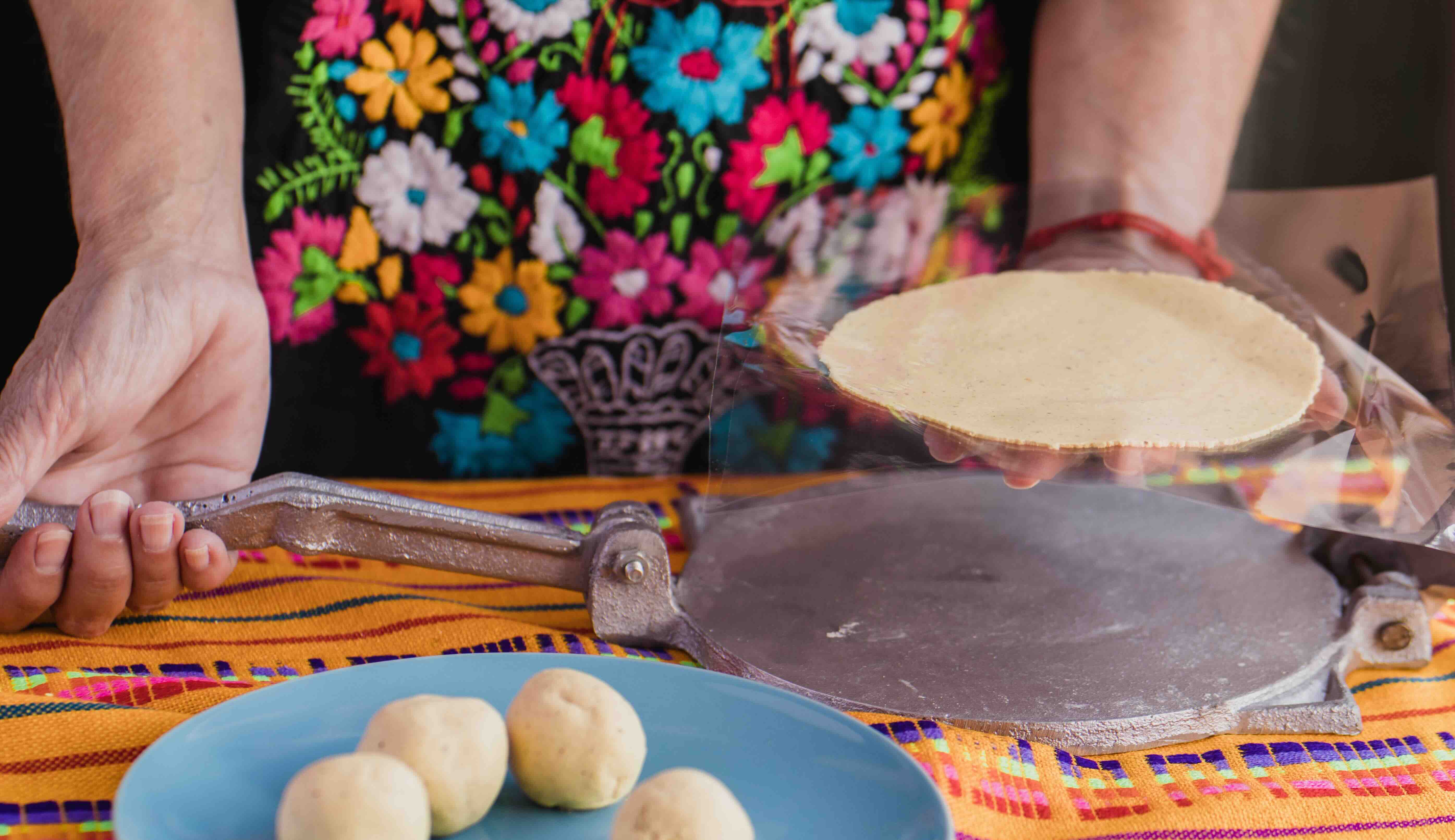 A woman makes tortillas using a tortilla press.