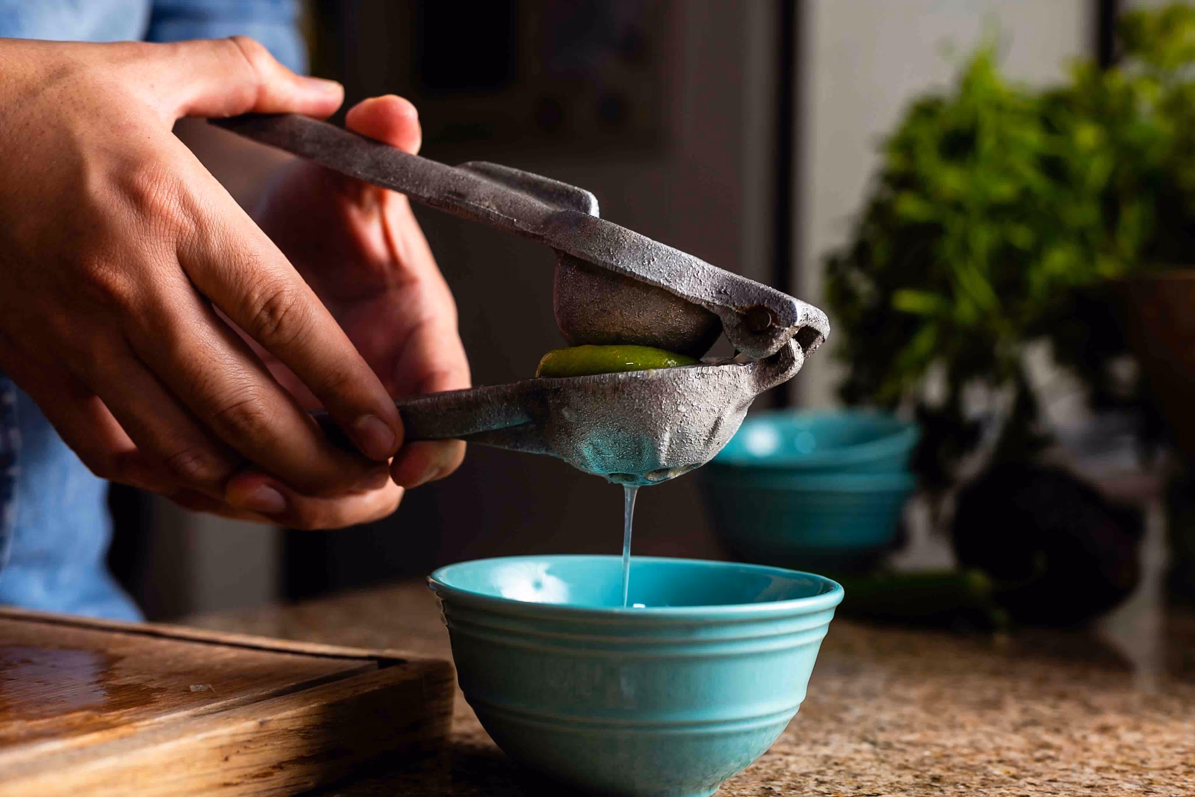 A man squeezes lime juice into a bowl with a lime press.