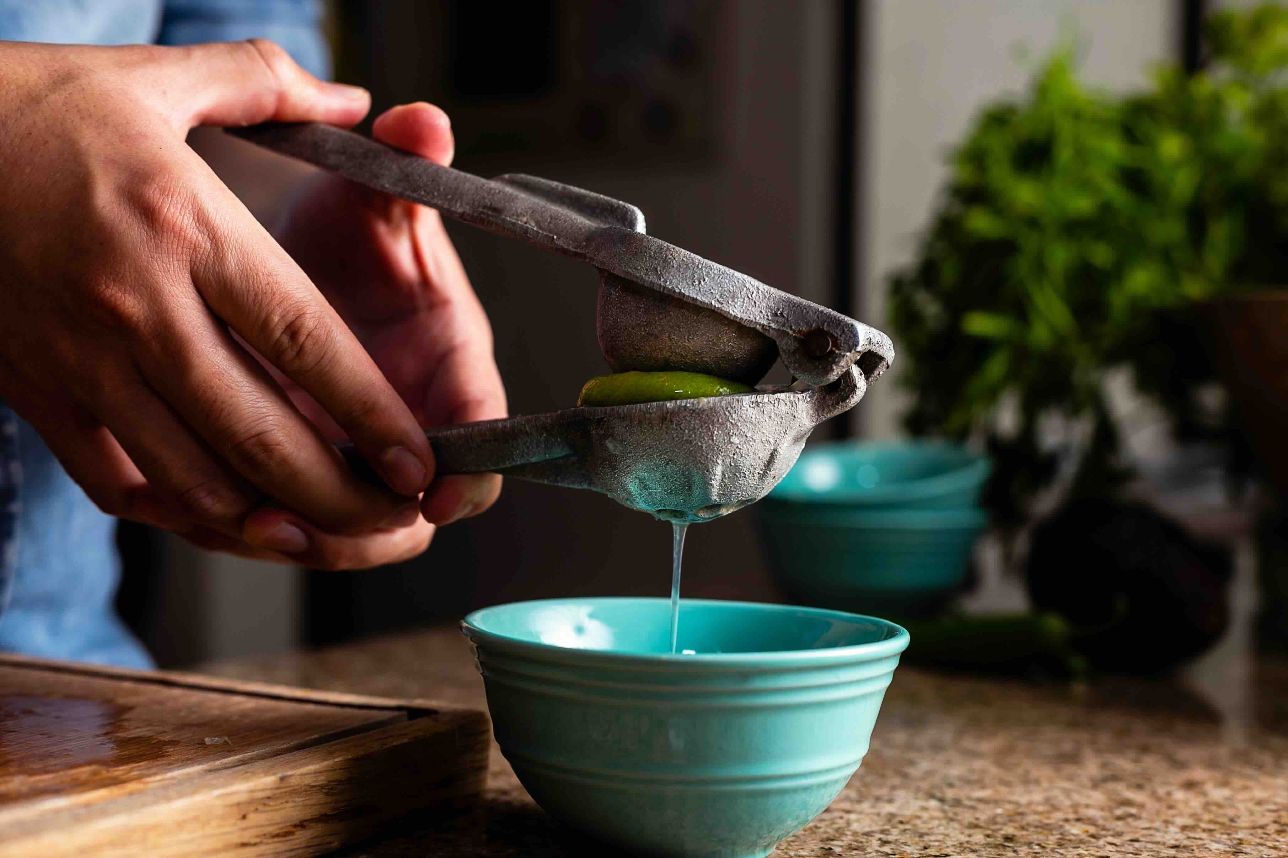 A man squeezes lime juice into a bowl using a lime press.
