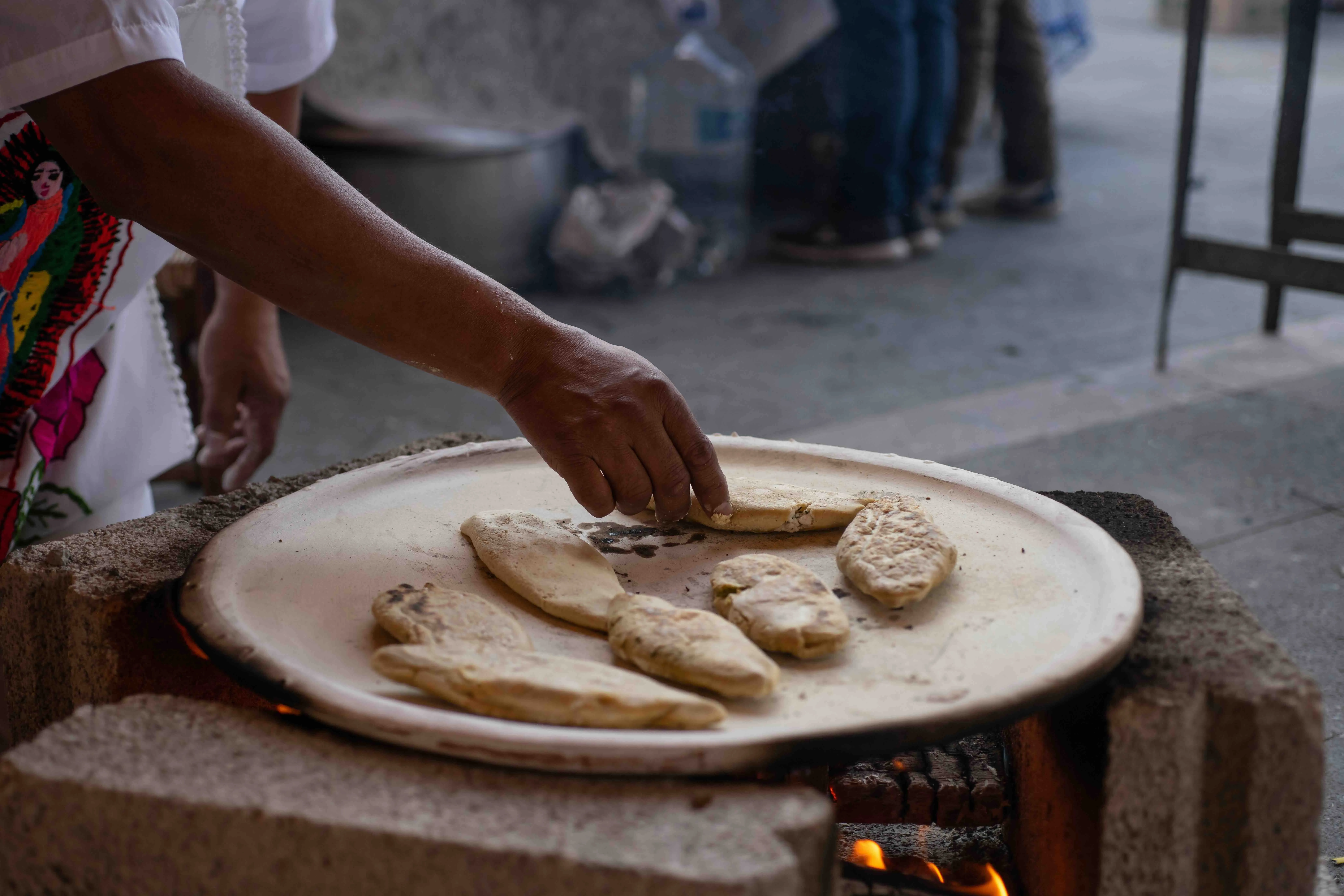A Mexican man cooking tlacoyos on a clay comal over a wood fire.