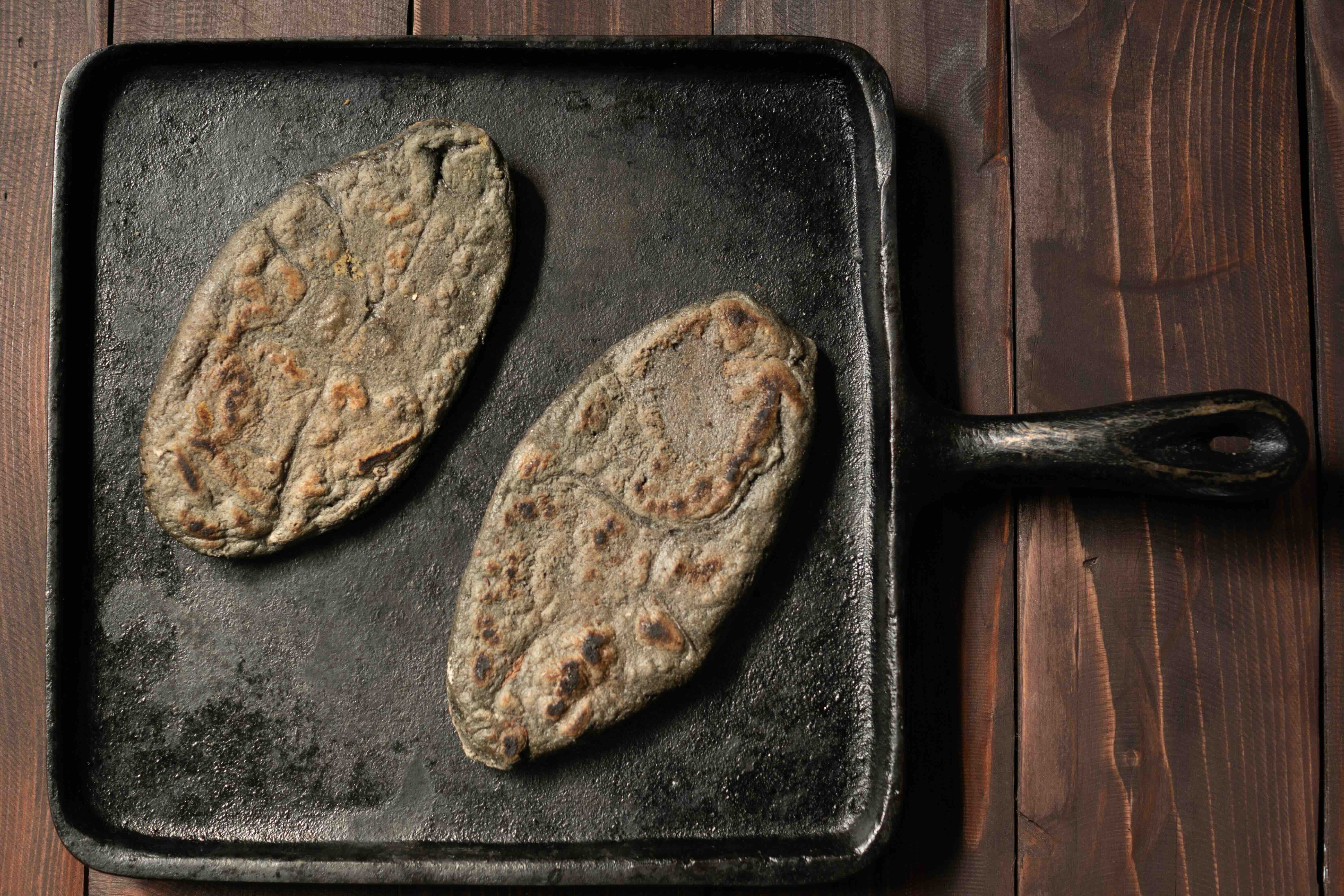 Blue corn tlacoyos on a cast iron comal.