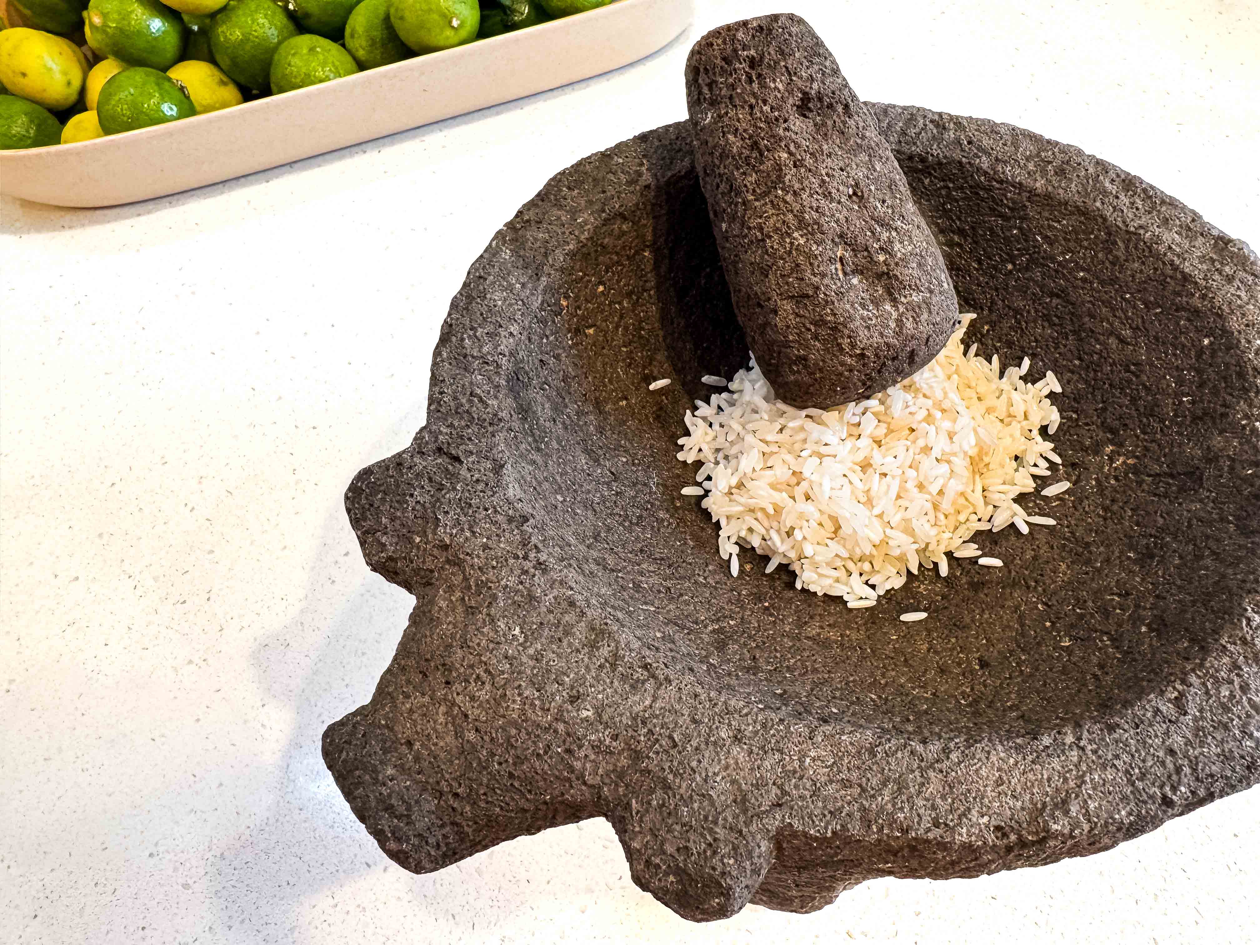 Some uncooked white rice sits in the molcajete with the tejolote, or pestal, resting on it.