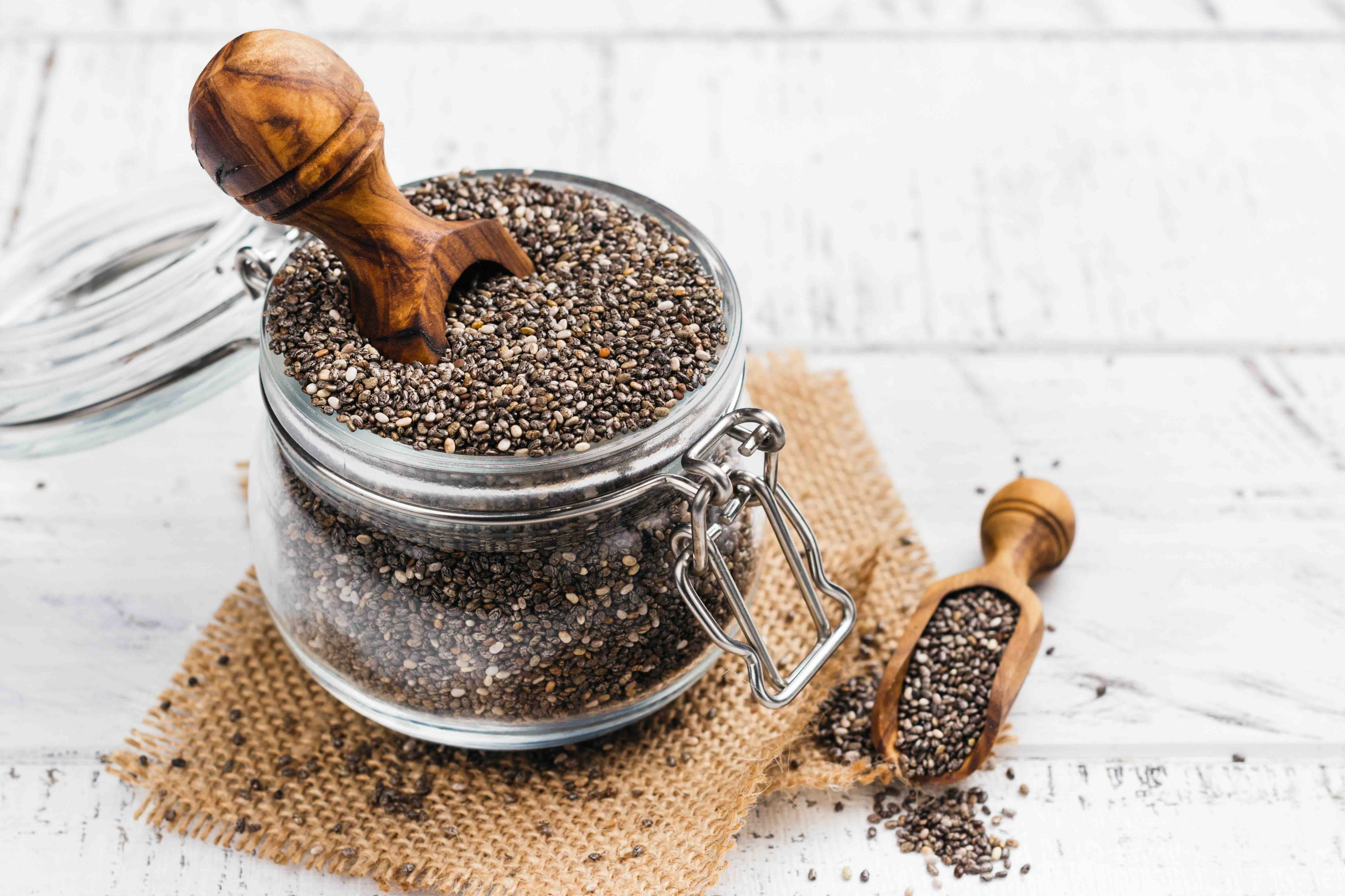 A small glass jar filled with chia seeds on top of a square of burlap.