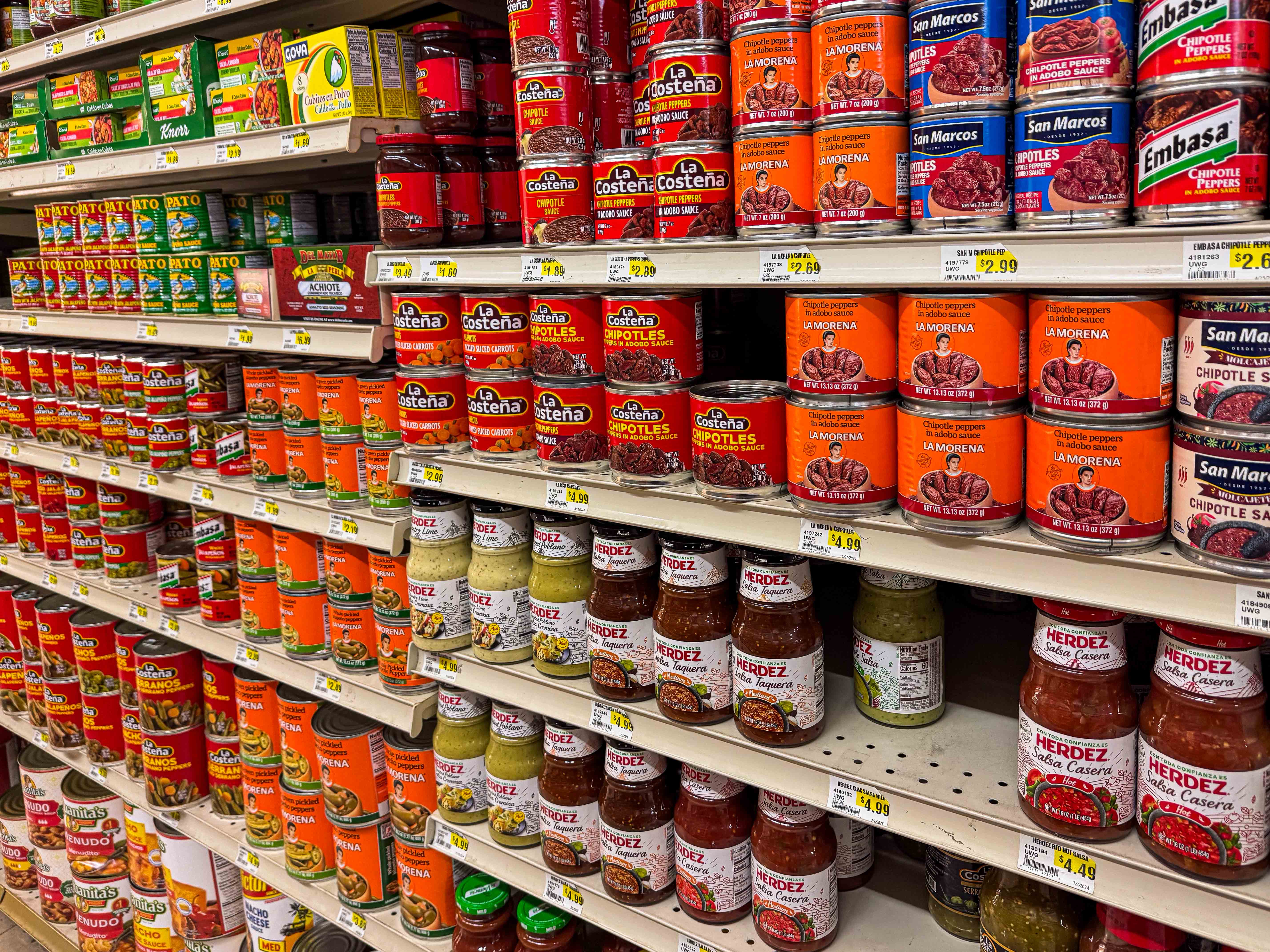 A variety of canned goods including salsas and chipotles in adobo in a grocery store.