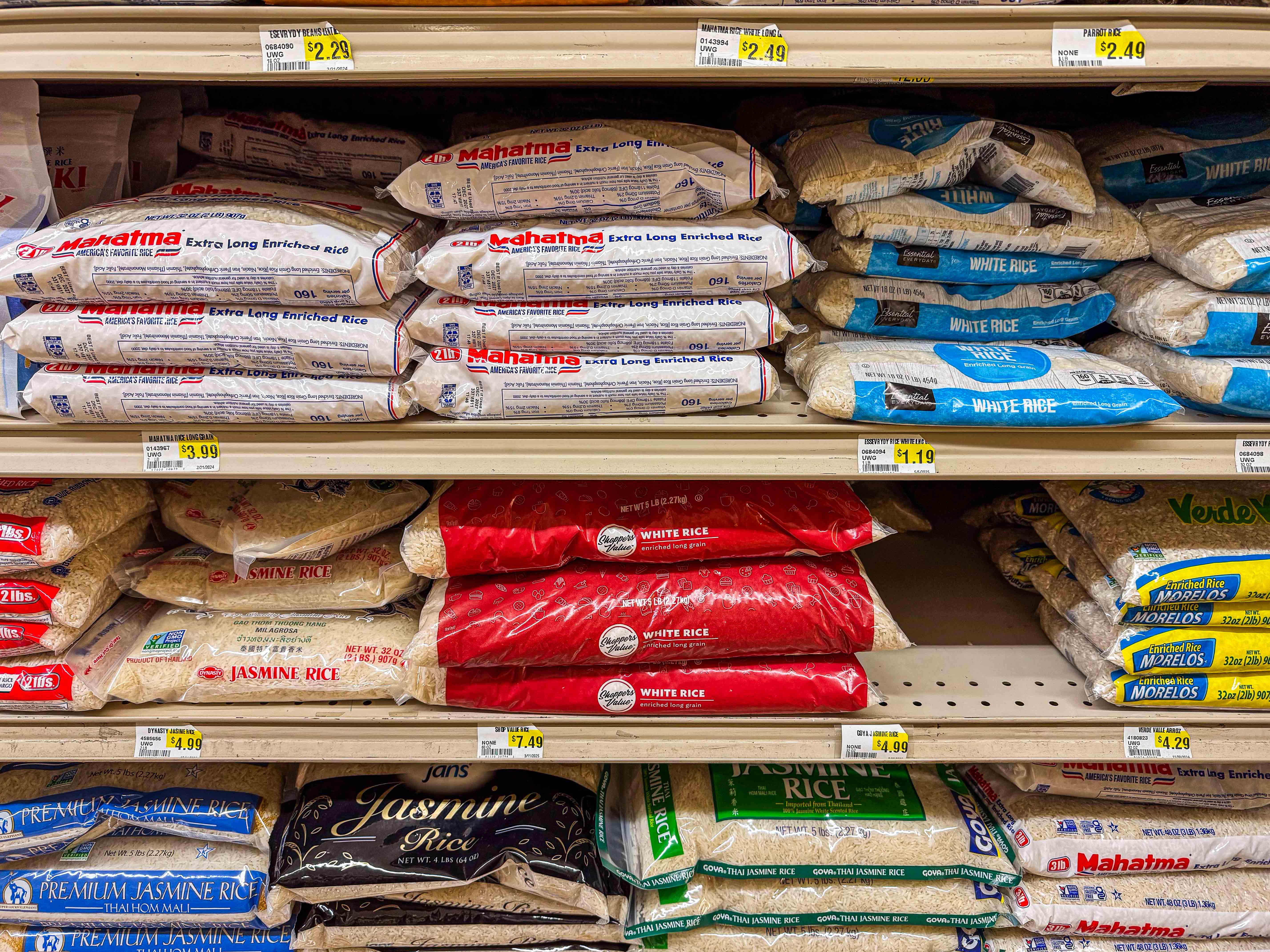 Many bags of different varieties of white rice resting on shelves in a grocery store.