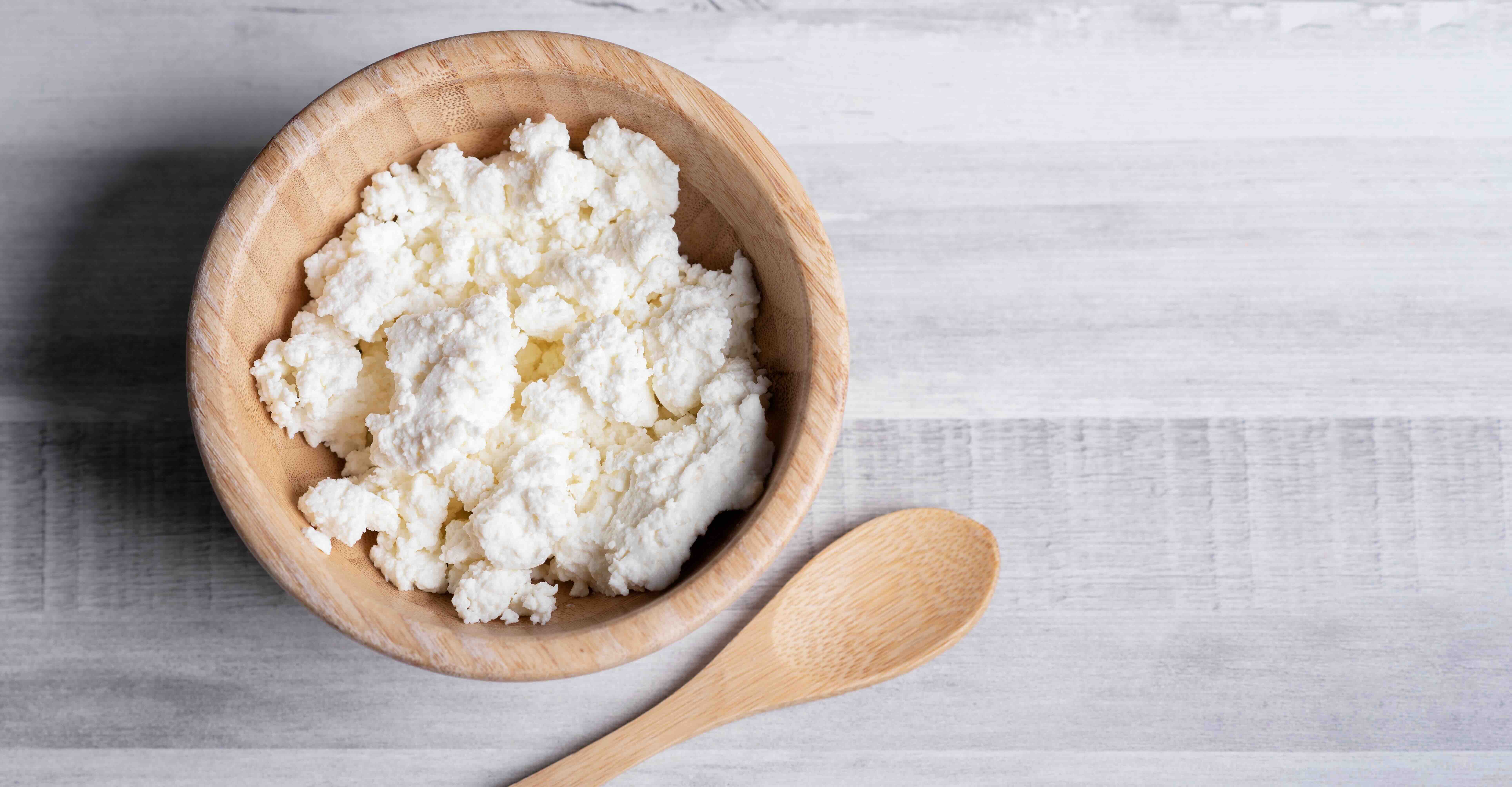 Queso requeson, a soft Mexican cheese, crumbled in a small wooden bowl with a wooden spoon resting on the gray wooden table. 