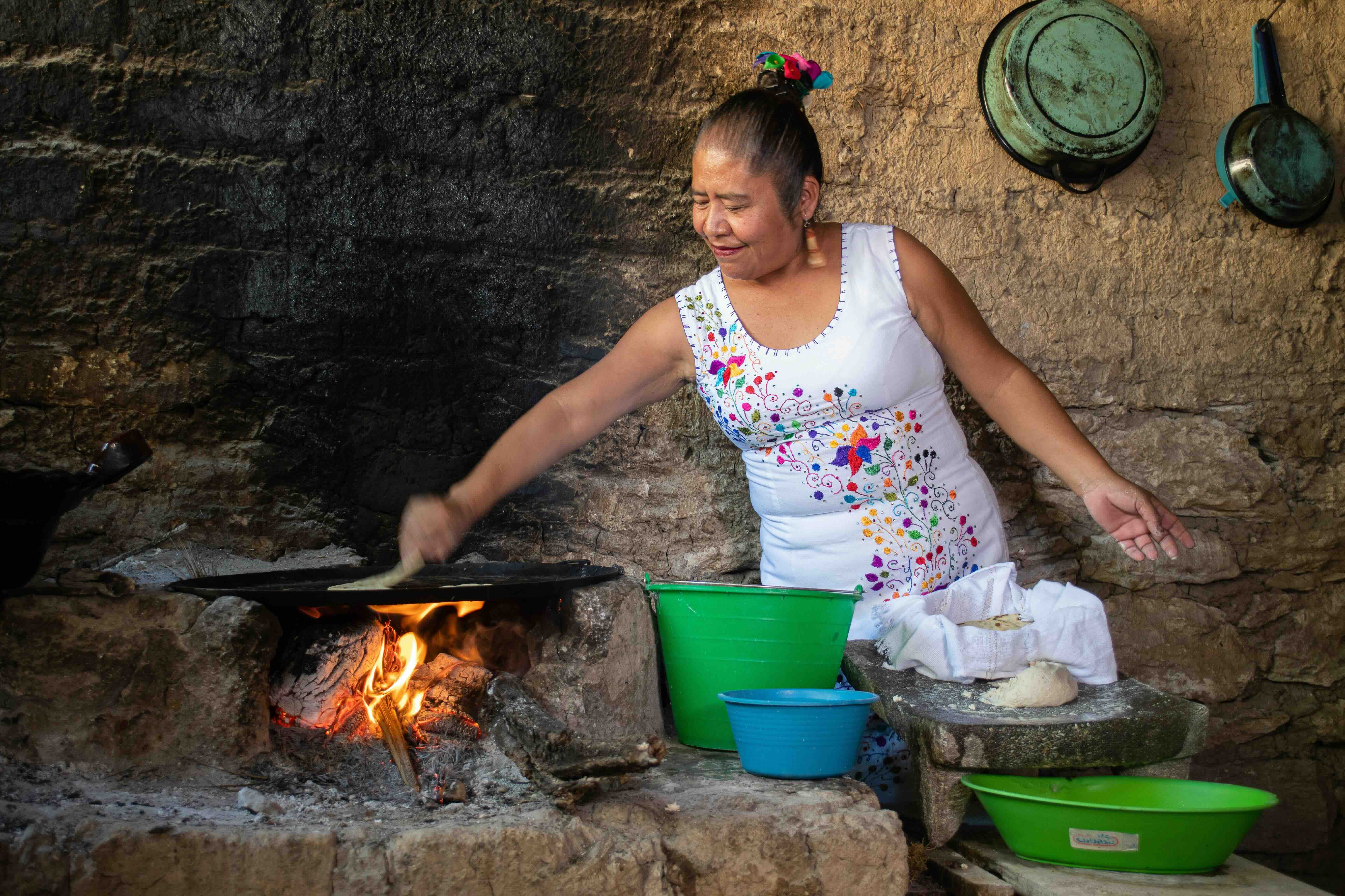 A woman making fresh tortillas with a metate and a comal over a wood fire.