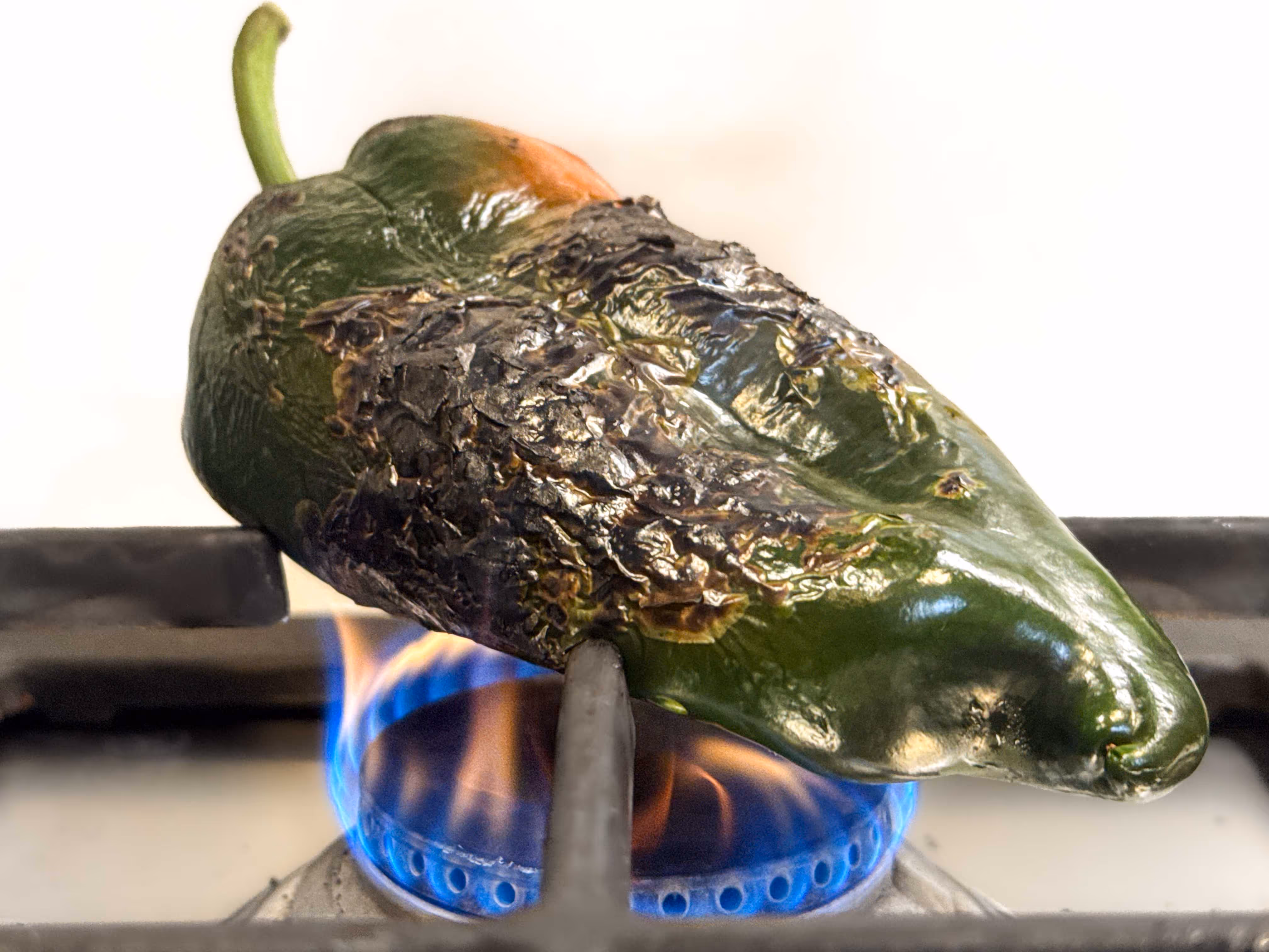 A charred poblano chile roasting on an open flame on the stove.