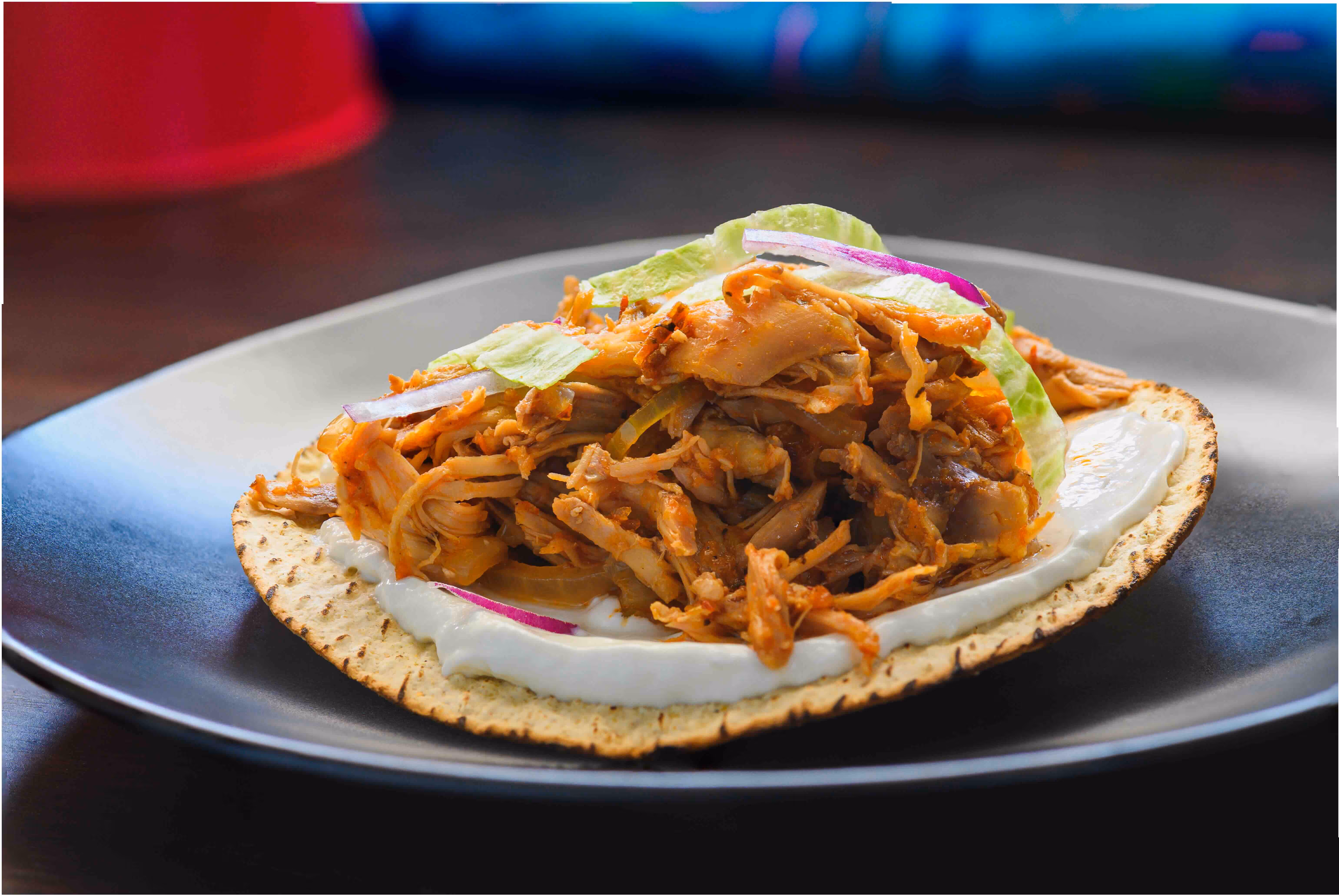 Close-up of a chicken tinga tostada garnished with crema, lettuce, and red onion on a black plate.