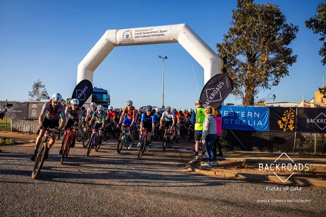 Riders under the Backroads Gravel start arch at dawn