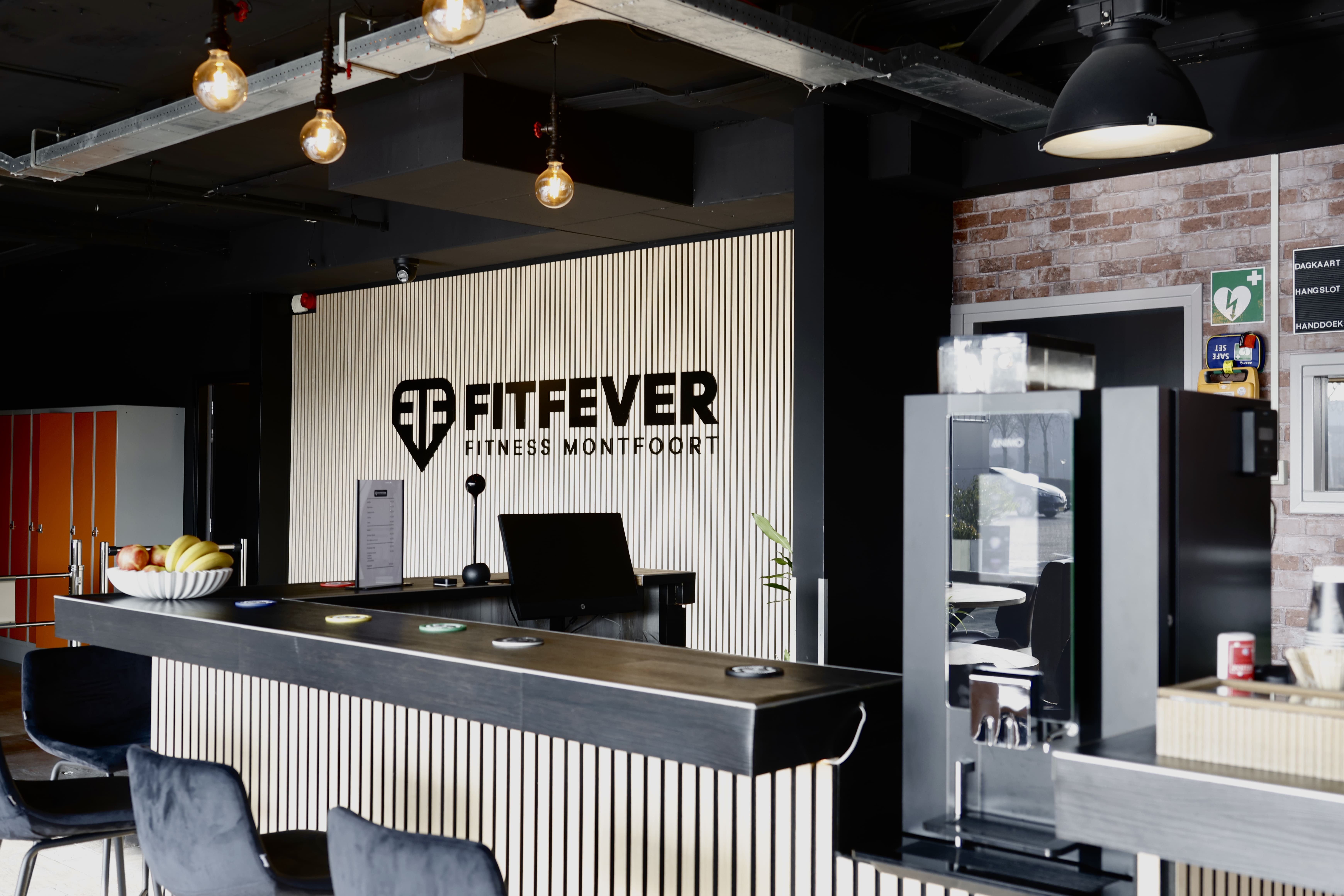 Reception area of Fittever Fitness Montfoort with black and white decor, a counter with chairs, and a bowl of fruit.