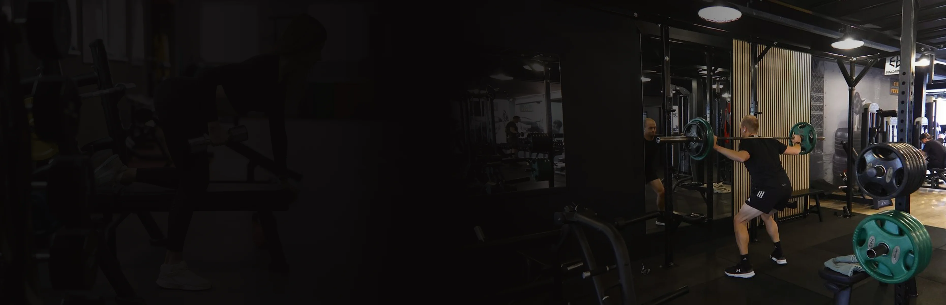 Man performing a barbell squat inside a gym with weights and fitness equipment.