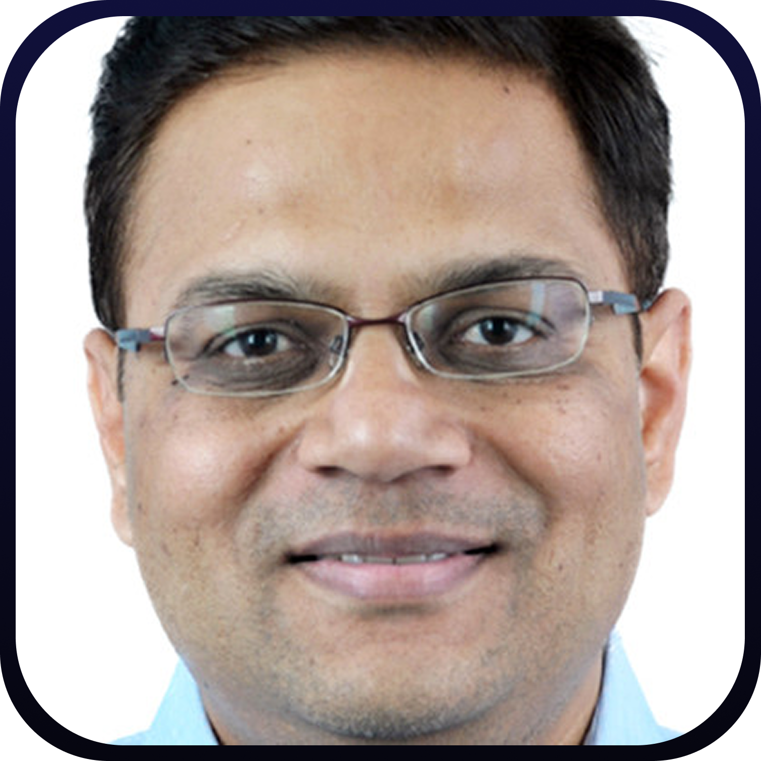 Close-up of a middle-aged man with short dark hair, glasses, and a light blue shirt smiling slightly.
