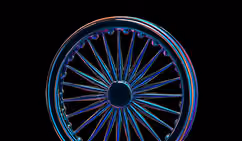 Close-up of a bicycle wheel with multicolored neon light reflections against a black background.