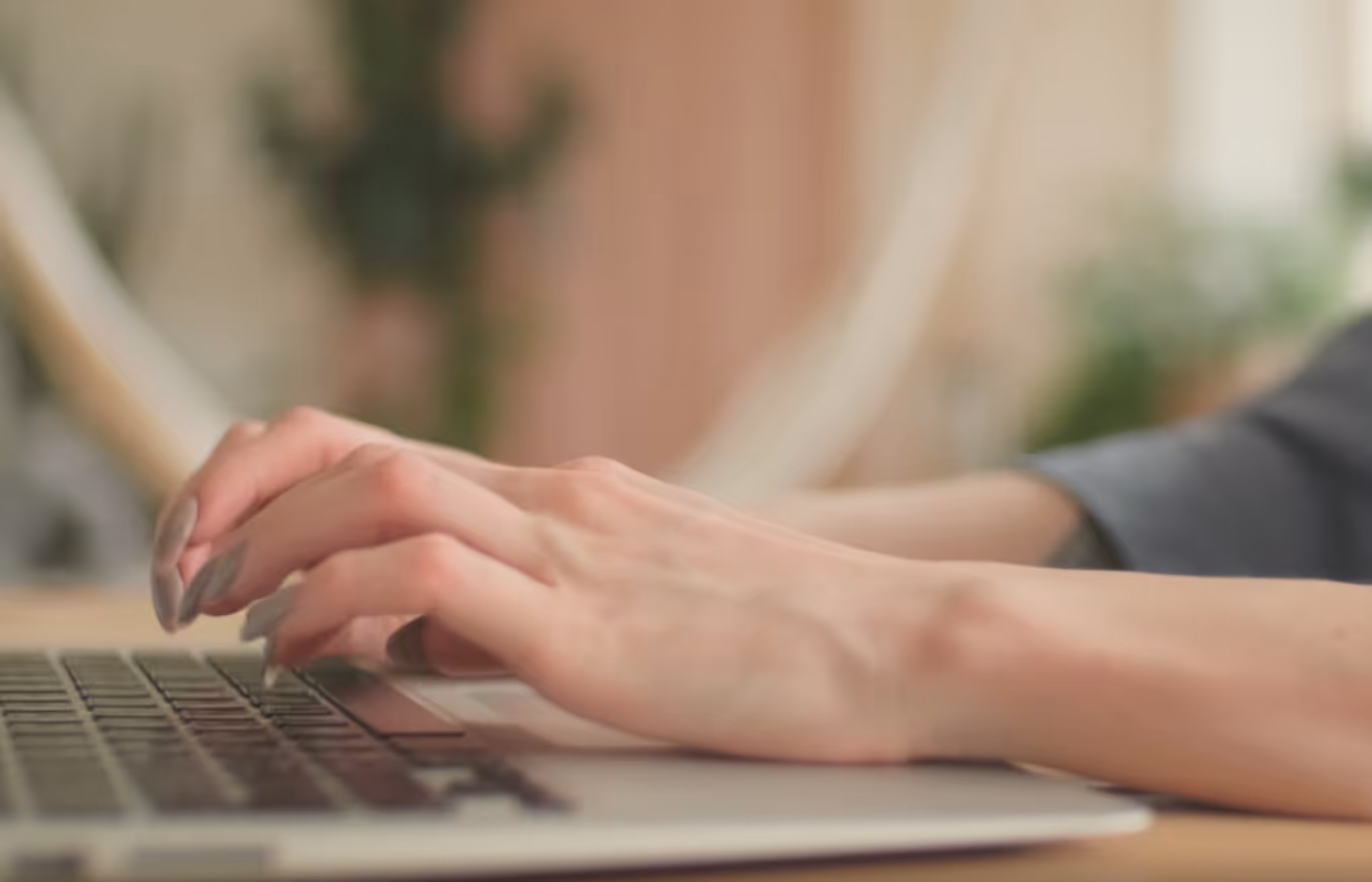 Woman's hands with manicured nails typing on a laptop keyboard.