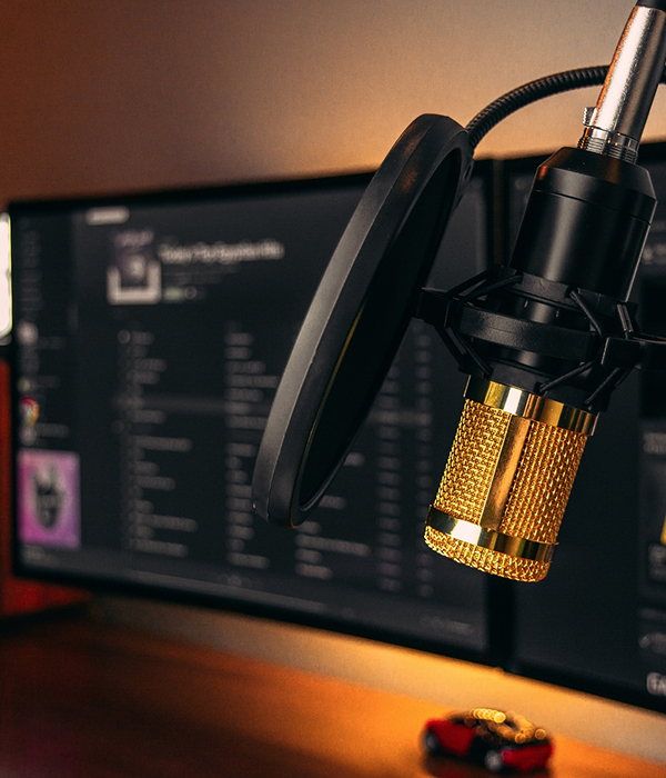 Close-up of a gold-colored condenser microphone with a pop filter in front of a computer screen displaying a music playlist.