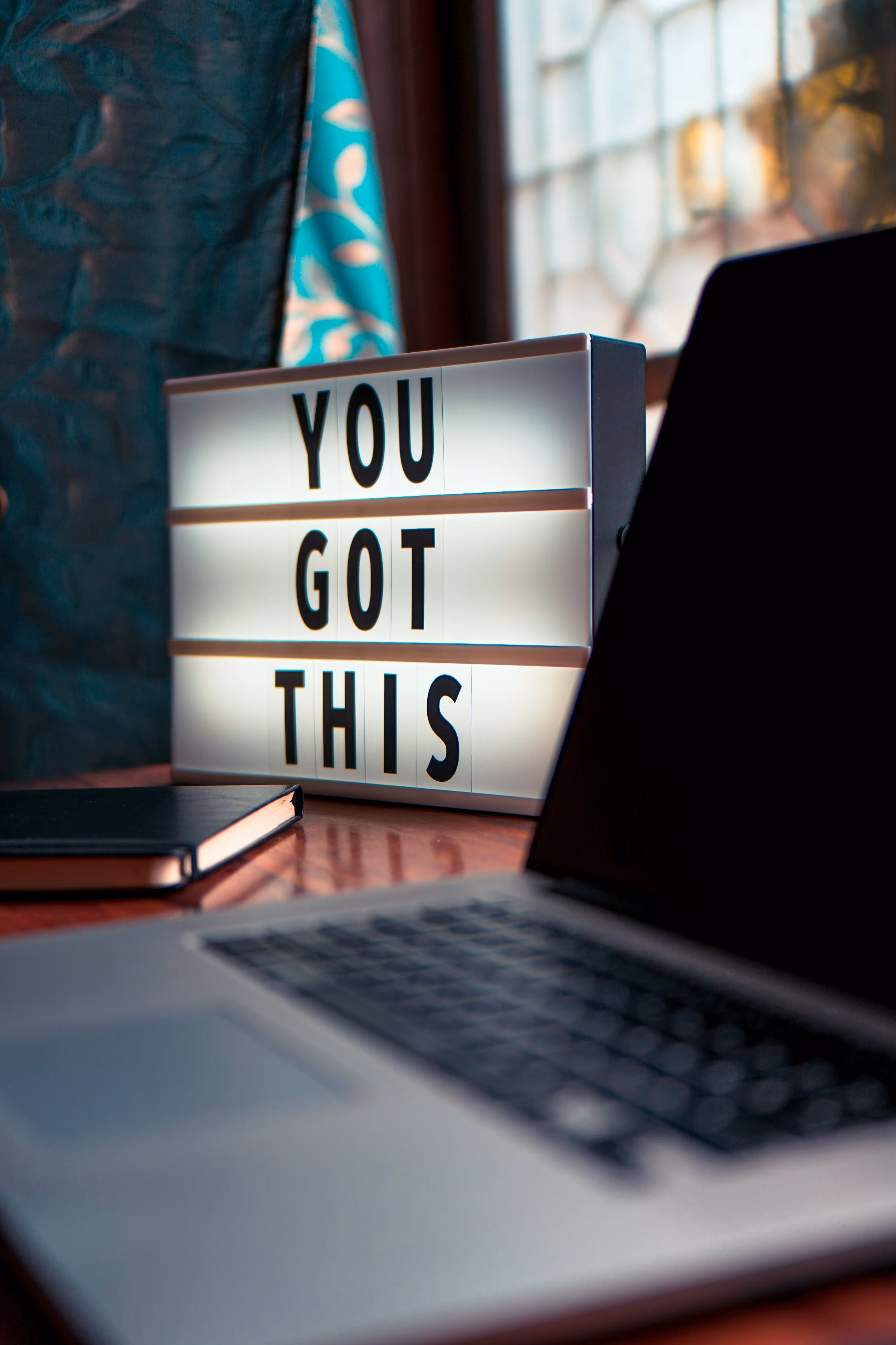 Lightbox on desk displaying motivational message 'YOU GOT THIS' beside a laptop and notebook.