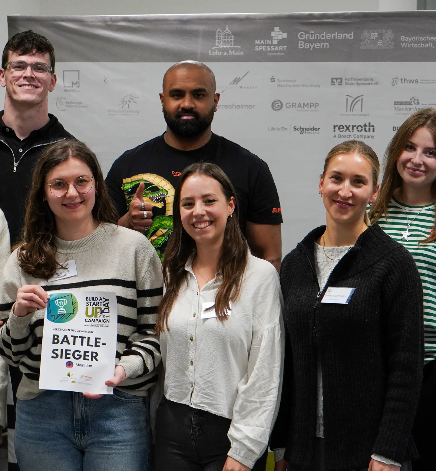 Gruppenfoto von sechs lächelnden jungen Erwachsenen, eine Frau hält eine Urkunde mit der Aufschrift ‚Battle-Sieger‘ bei einer Veranstaltung.