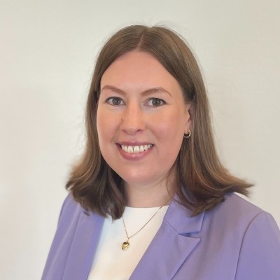Smiling woman with curly red hair wearing a blue denim shirt outdoors in a residential area.
