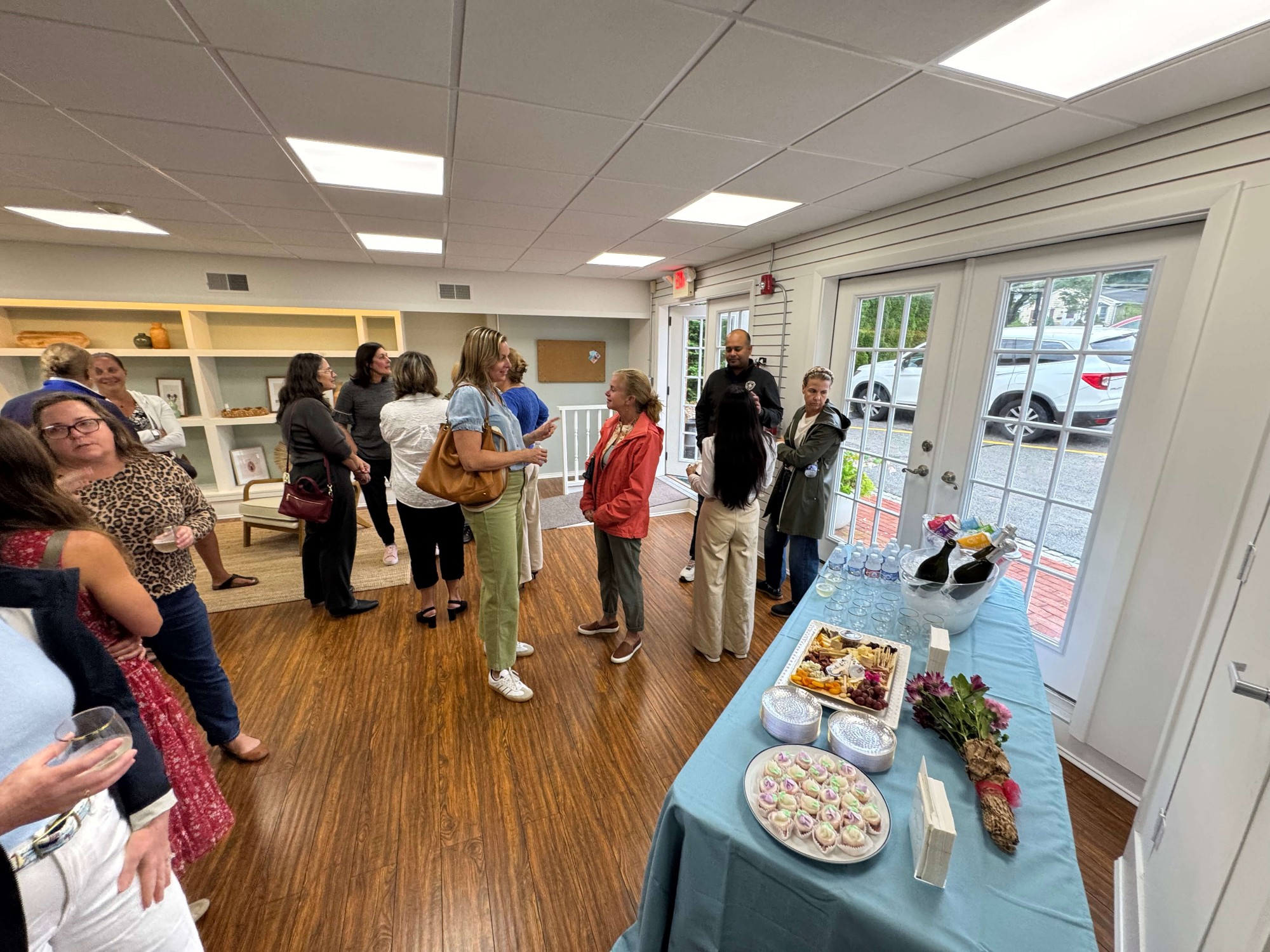 Group of people socializing indoors near a table with snacks, drinks, and flowers.
