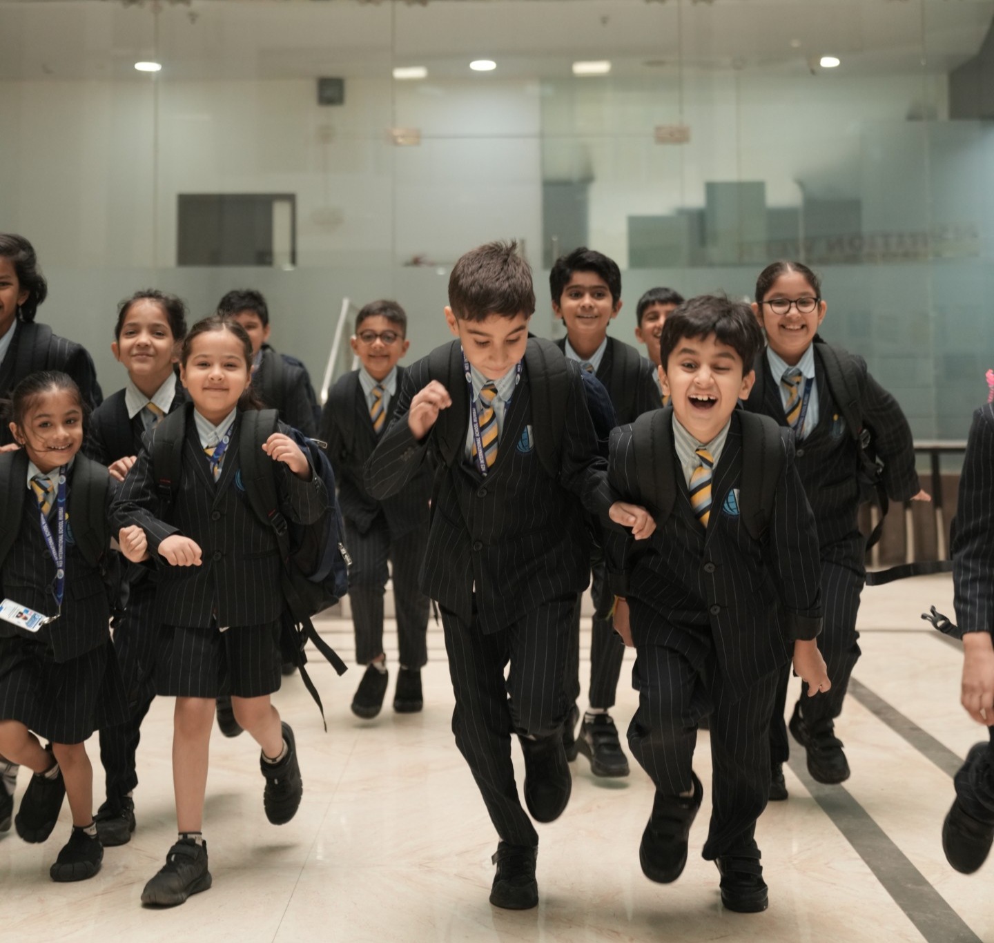 Group of schoolchildren in striped uniforms joyfully running indoors with backpacks.