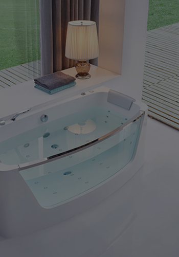 Modern bathtub with water, headrest, lamp, and folded towels near a glass door to a wooden deck.
