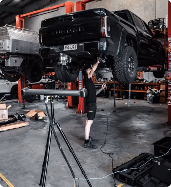 Mechanic working under a lifted black Toyota Tundra truck in an auto repair shop.
