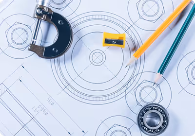 Mechanical drafting tools including a micrometer, pencil sharpener, pencils, and a bearing placed on a technical blueprint drawing.
