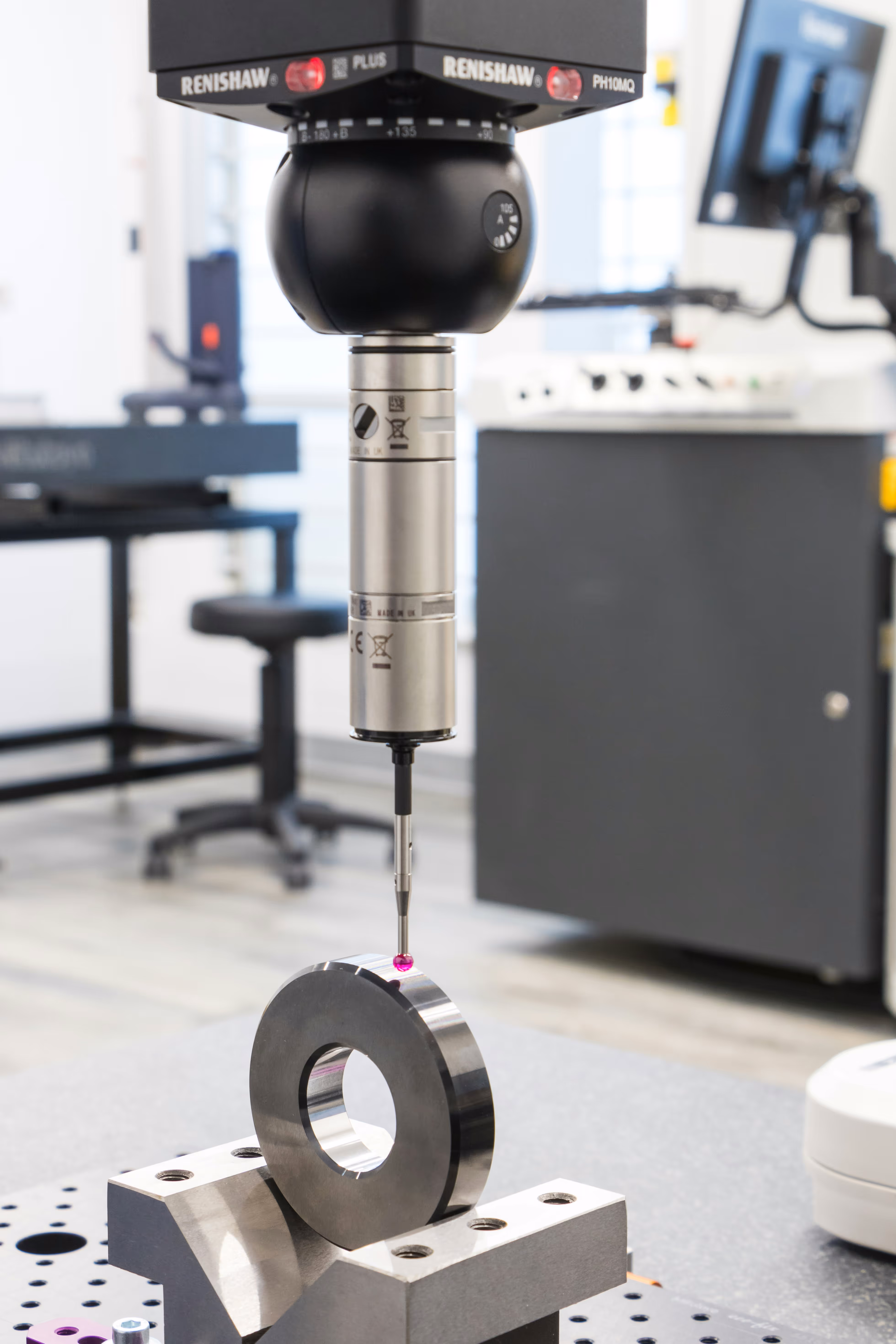 Precision measuring device with a probe touching a metallic ring held in a fixture in a laboratory setting.
