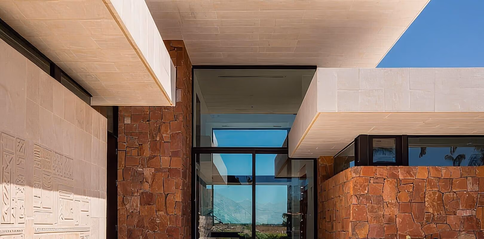 Modern luxury home exterior with stone walls, cantilevered concrete slabs, and glass entrance framing mountain views.