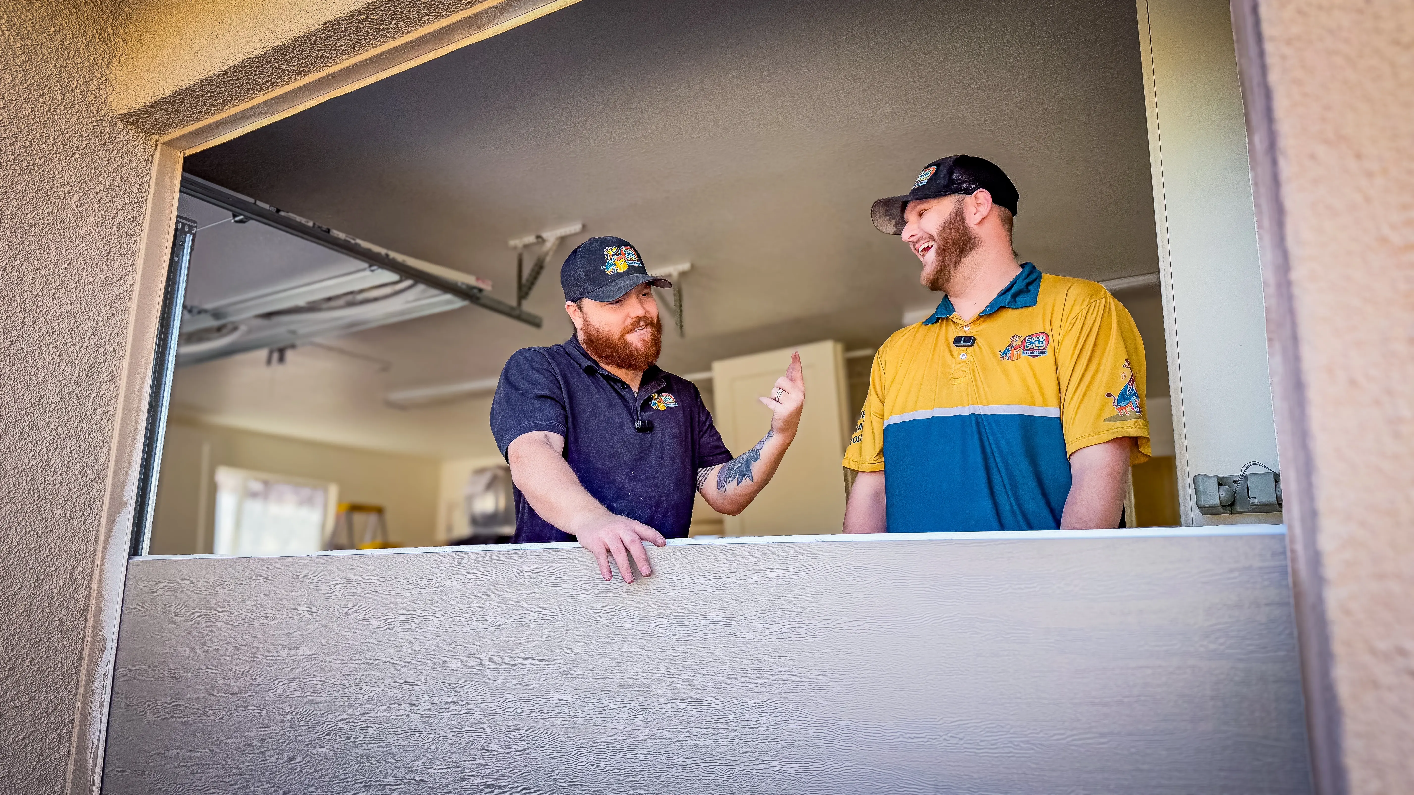Two men are smiling and chatting while standing in a garage.