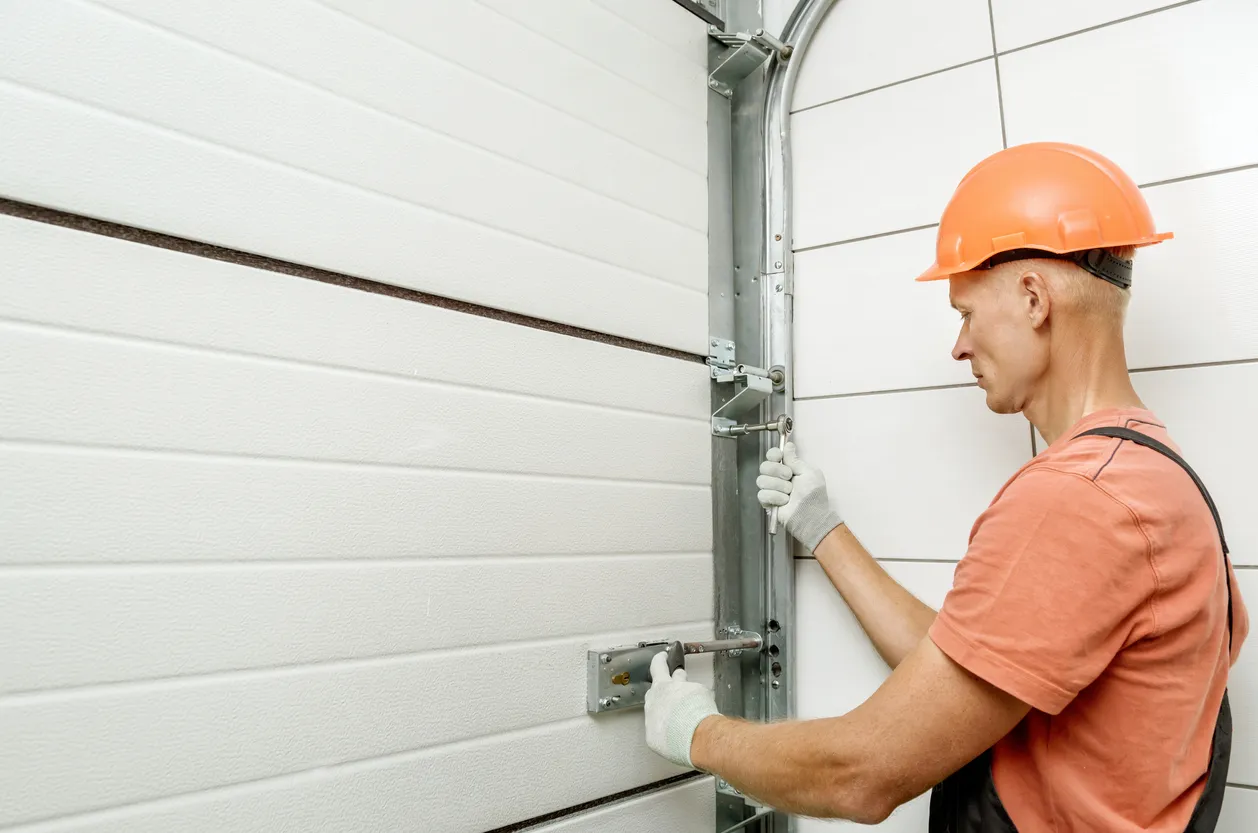 A man in safety gear adjusts the locking mechanism and tracks of a white garage door