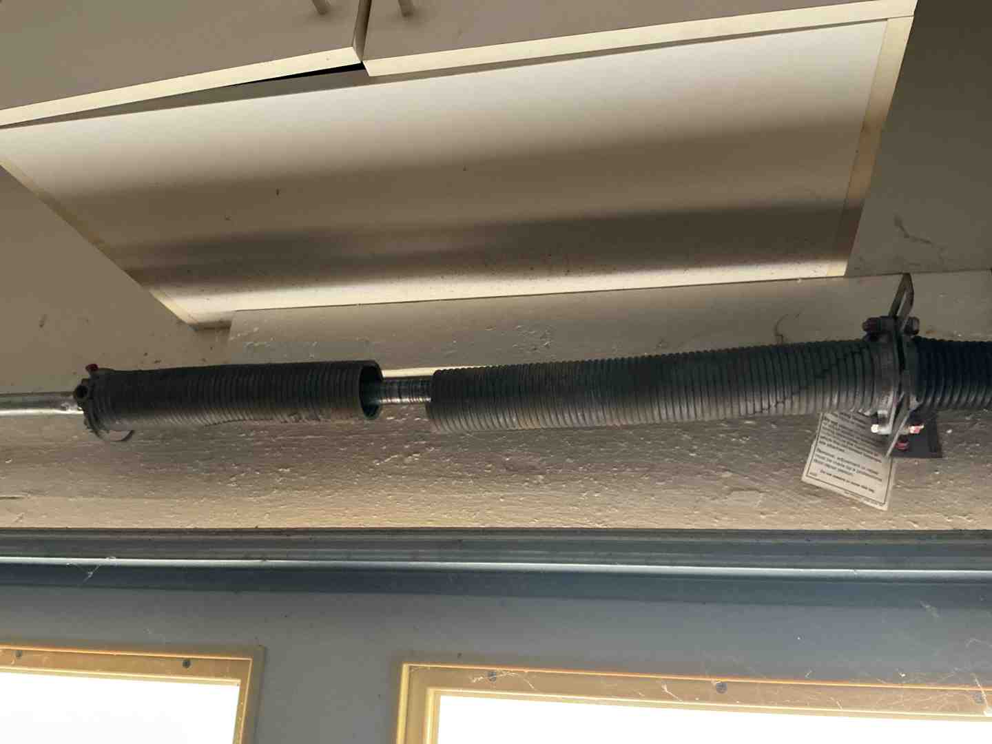 A snapped garage door torsion spring showing a visible gap in the metal coils - emergency garage door replacement in round
