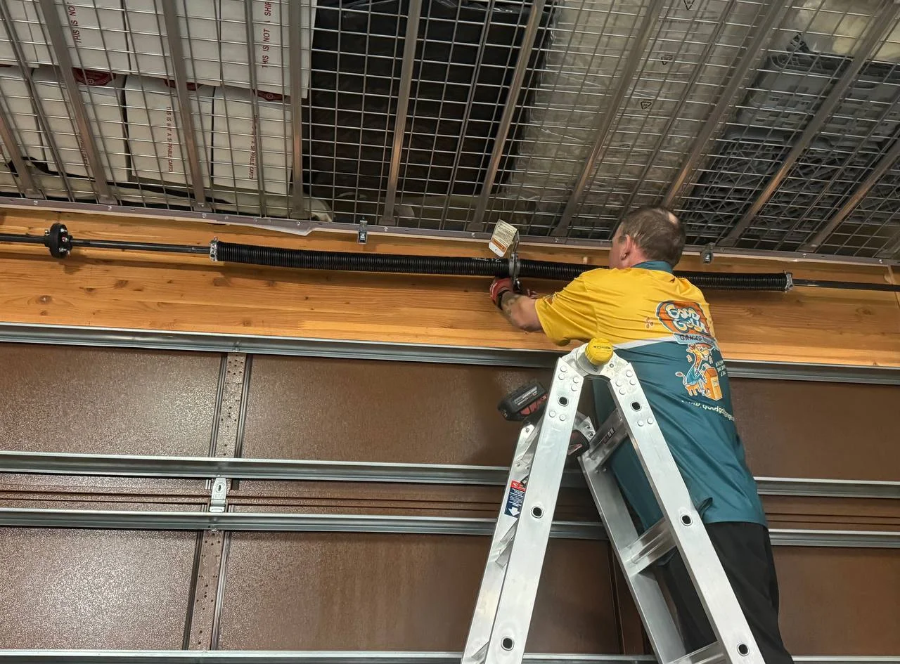 Technician in a garage inspecting a large silver torsion spring above the door with professional tools - how often should