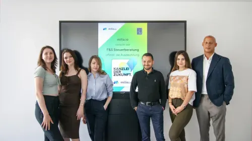 Group of six professionals standing in front of a display screen with a certification announcement from milia.io for F&S Steuerberatung.