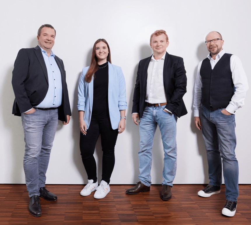 Die vier Partner der Kanzlei Scanlan & Partner stehen nebeneinander vor einer hellen Wand und lächeln in die Kamera.