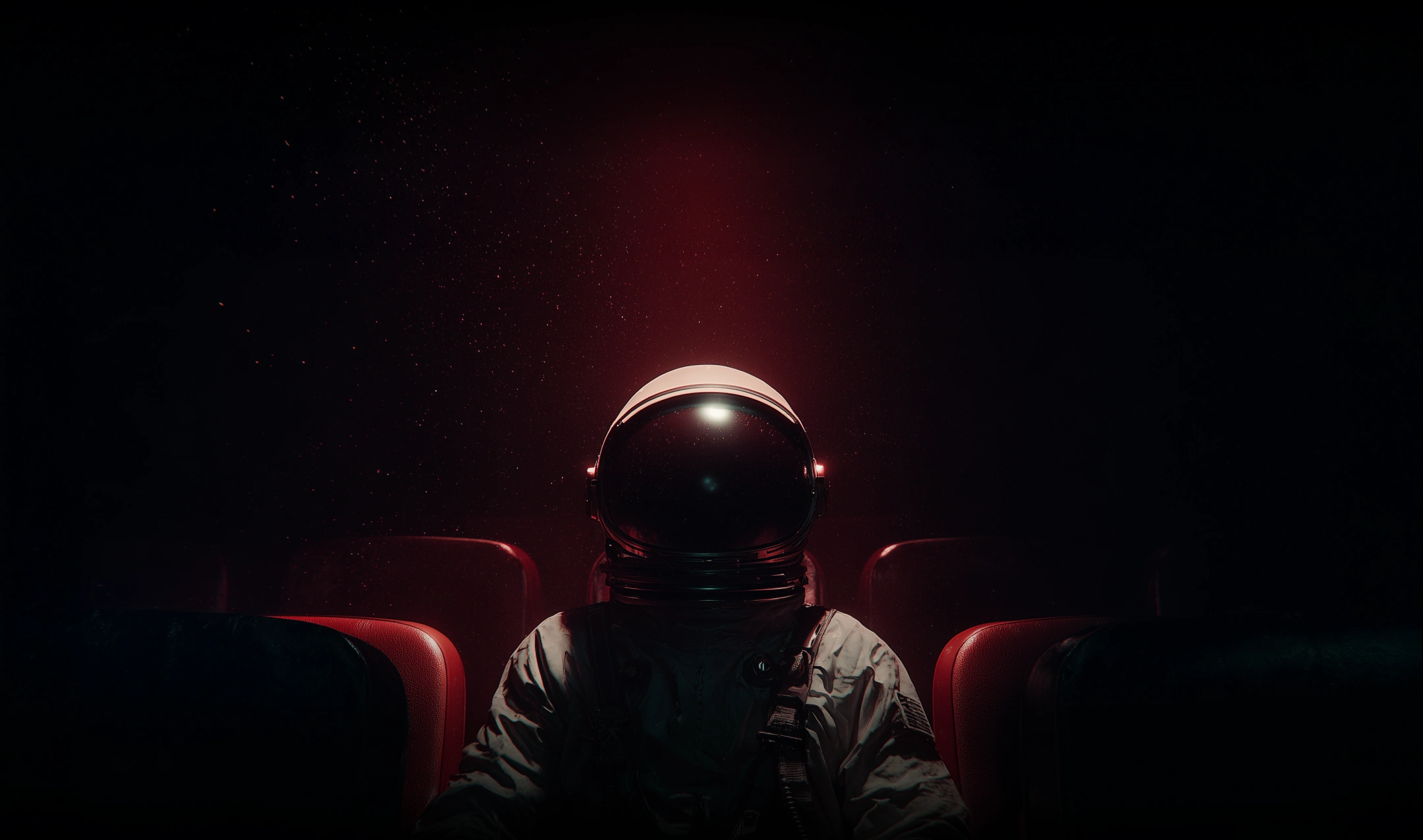 An astronaut sitting alone in a dark theater with red seats and a faint red glow behind.