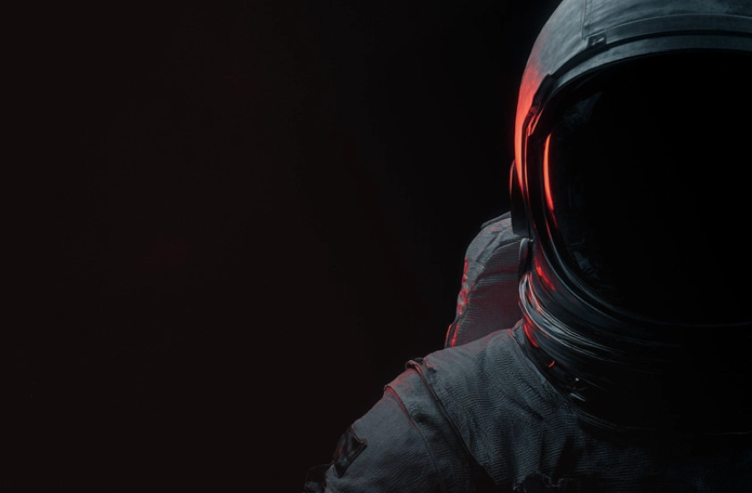 Close-up of an astronaut in a space suit with a dark visor against a black background, illuminated by red light on one side.