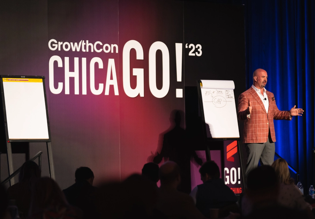 Speaker in a brown checkered blazer presenting on stage at GrowthCon CHICAGO ’23 with attendees in front.