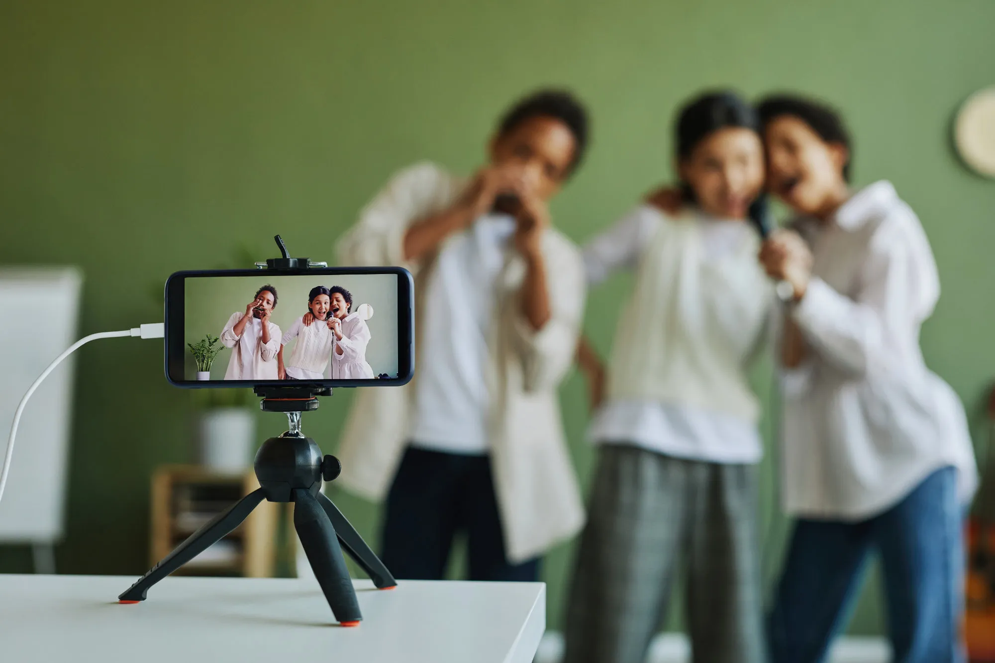 Three friends singing and recording a video together on a smartphone mounted on a tripod.