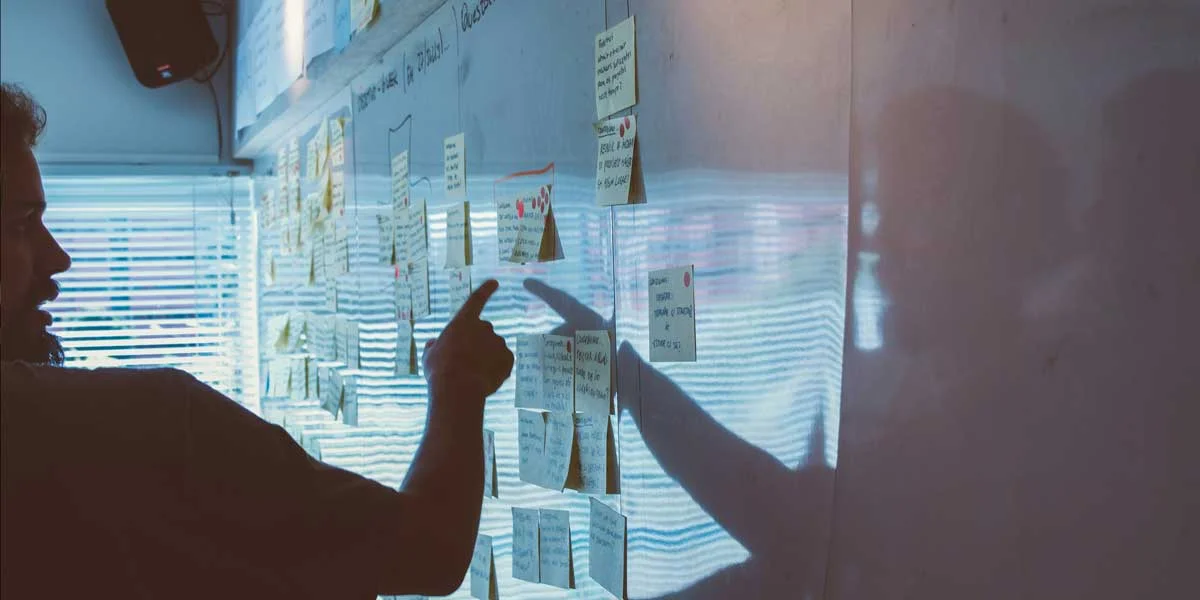 A man writing on a board with sticky notes on it