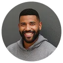 Smiling man with short hair and beard wearing a gray hoodie against a dark background.