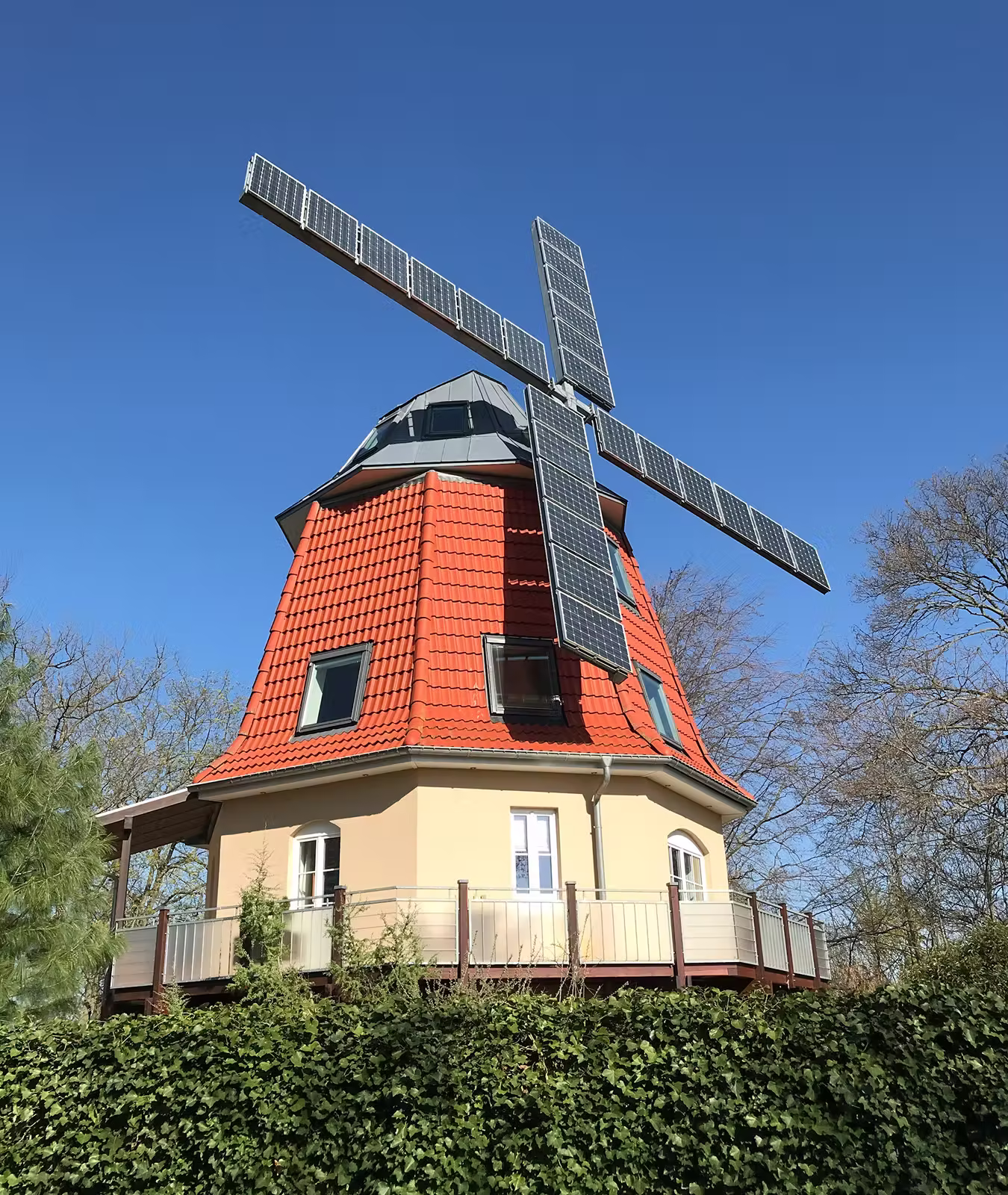 Windmill with solar panel blades on a red tiled roof against a clear blue sky.