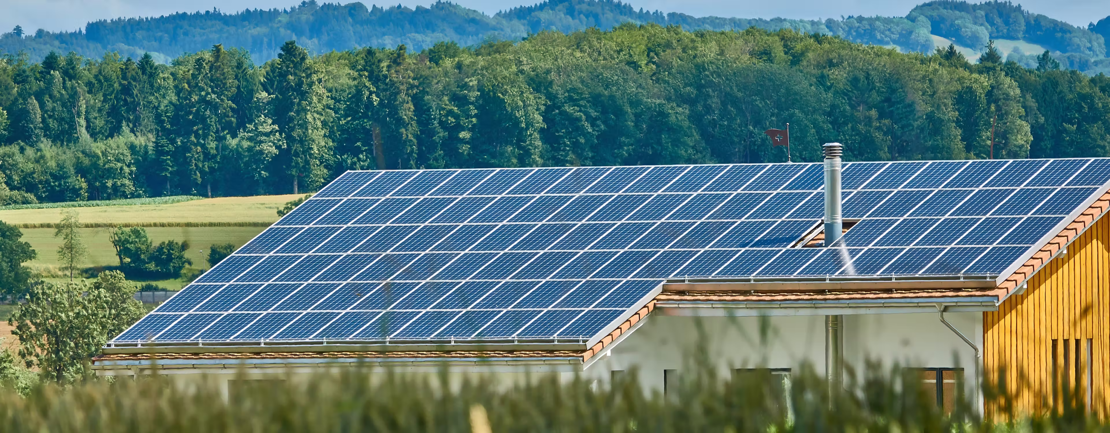 Rooftop covered with solar panels on a house surrounded by a green forest and hills.